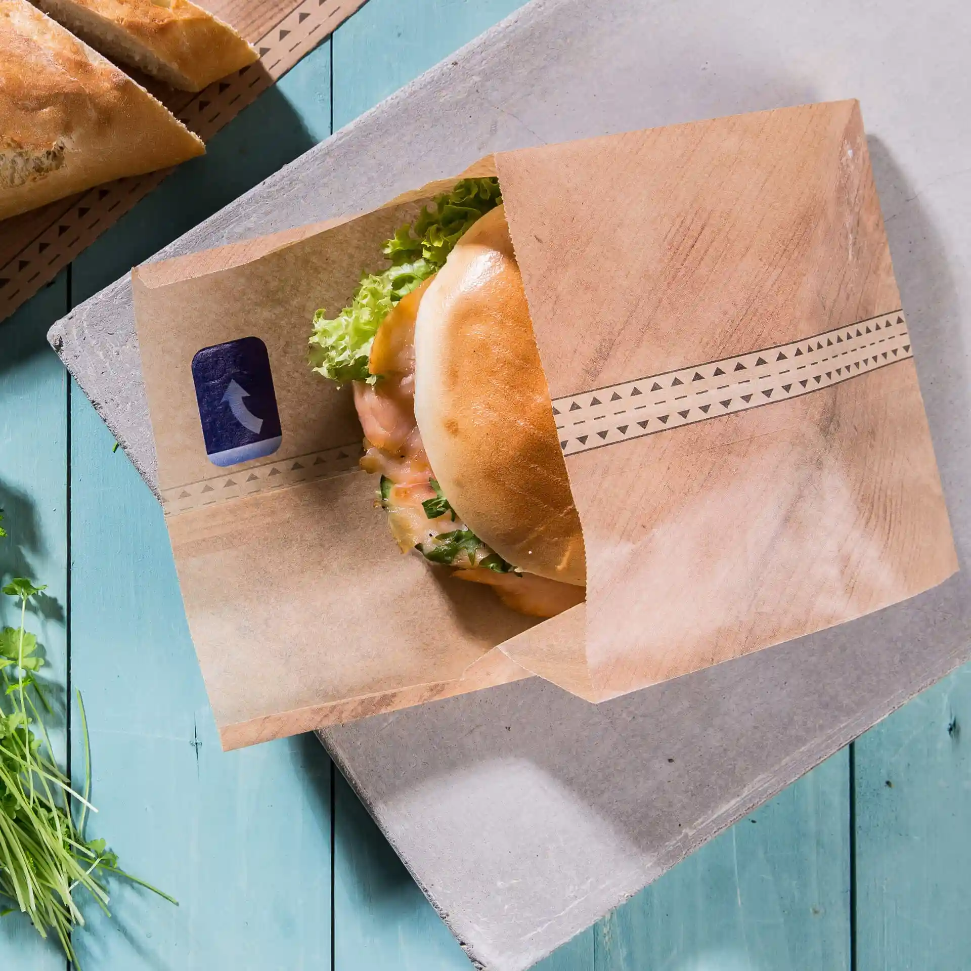 Sac en papier brun contenant un burger avec de la laitue, posé sur une surface en bois bleu.