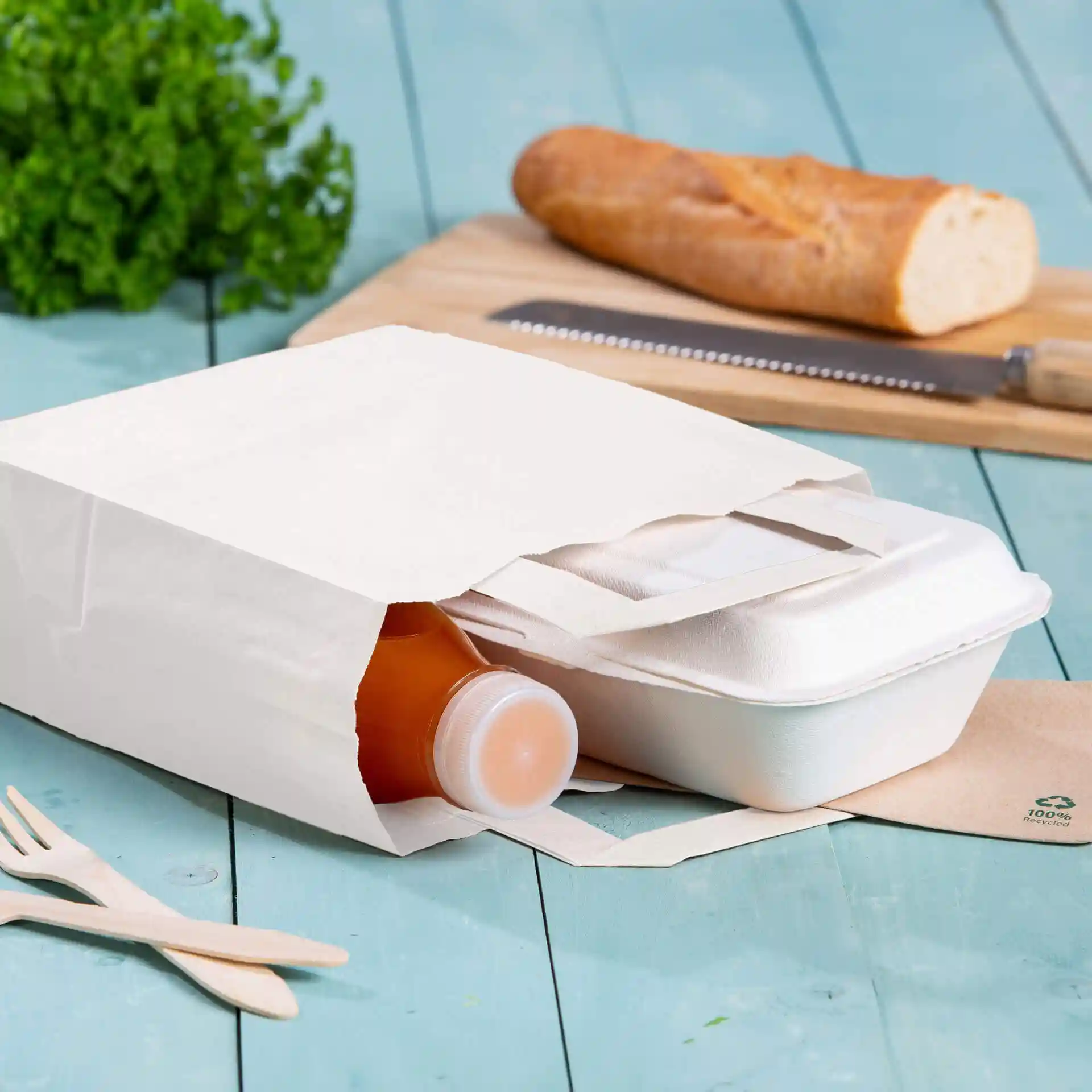 Sac en papier kraft blanc contenant une bouteille et un contenant à emporter, posé sur une surface en bois bleu.