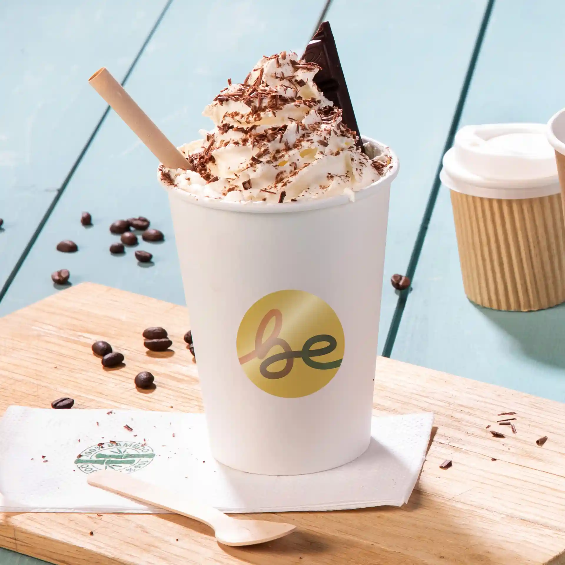 Tasse avec de la crème fouettée, des copeaux de chocolat et un morceau de chocolat, posée sur une surface en bois avec des grains de café.