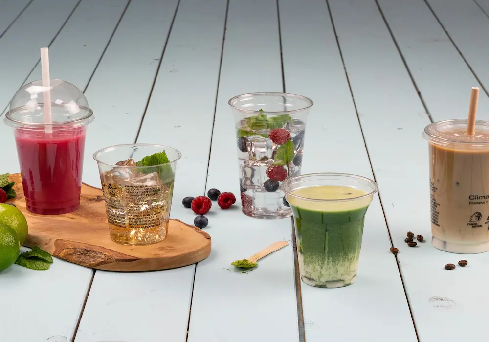 Cinq verres de différentes boissons sur un plateau en bois, avec des boissons roses, vertes, claires et brunes, des fruits et de la menthe.