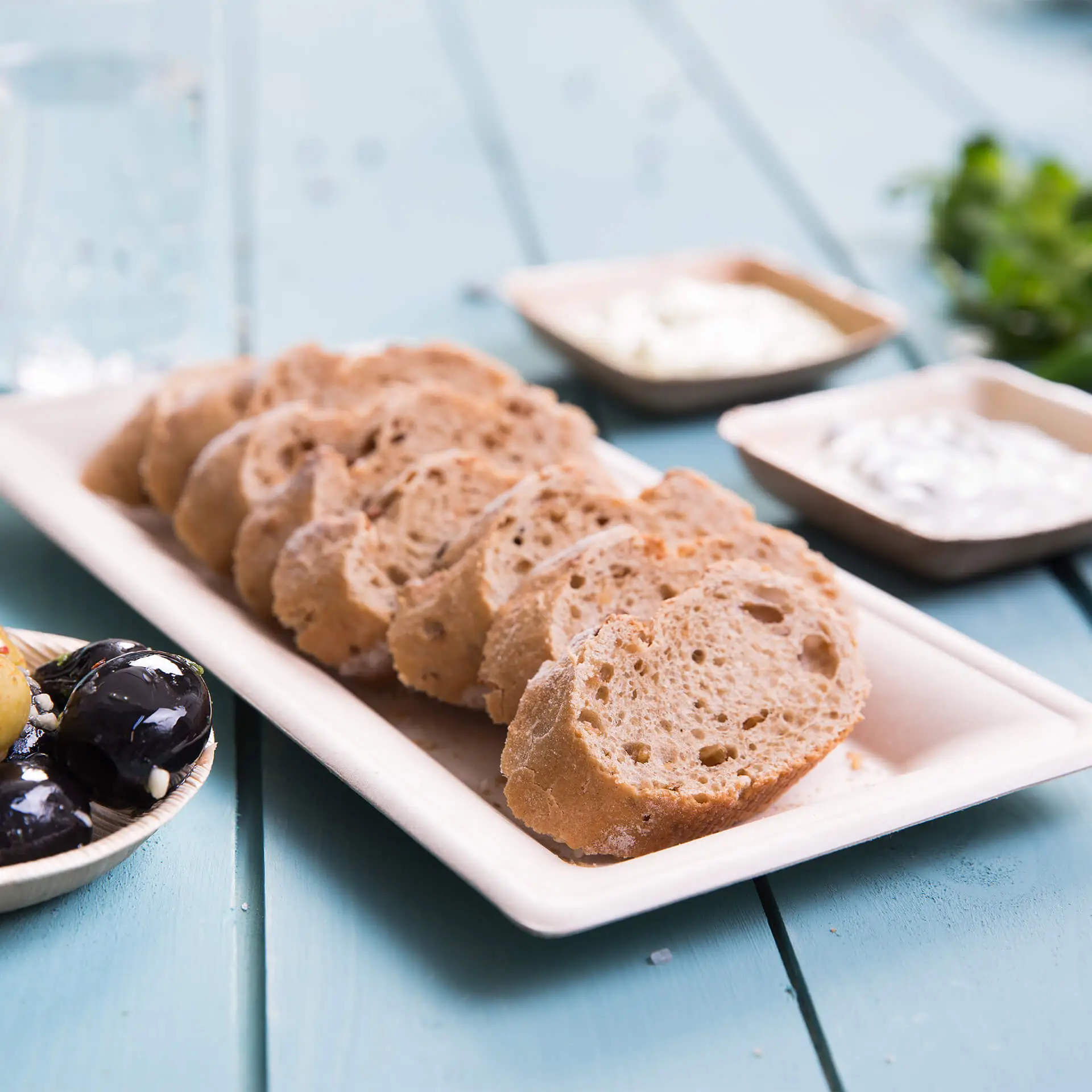 Pain tranché servi sur une assiette rectangulaire en canne à sucre, avec des dips dans de petits bols à proximité.