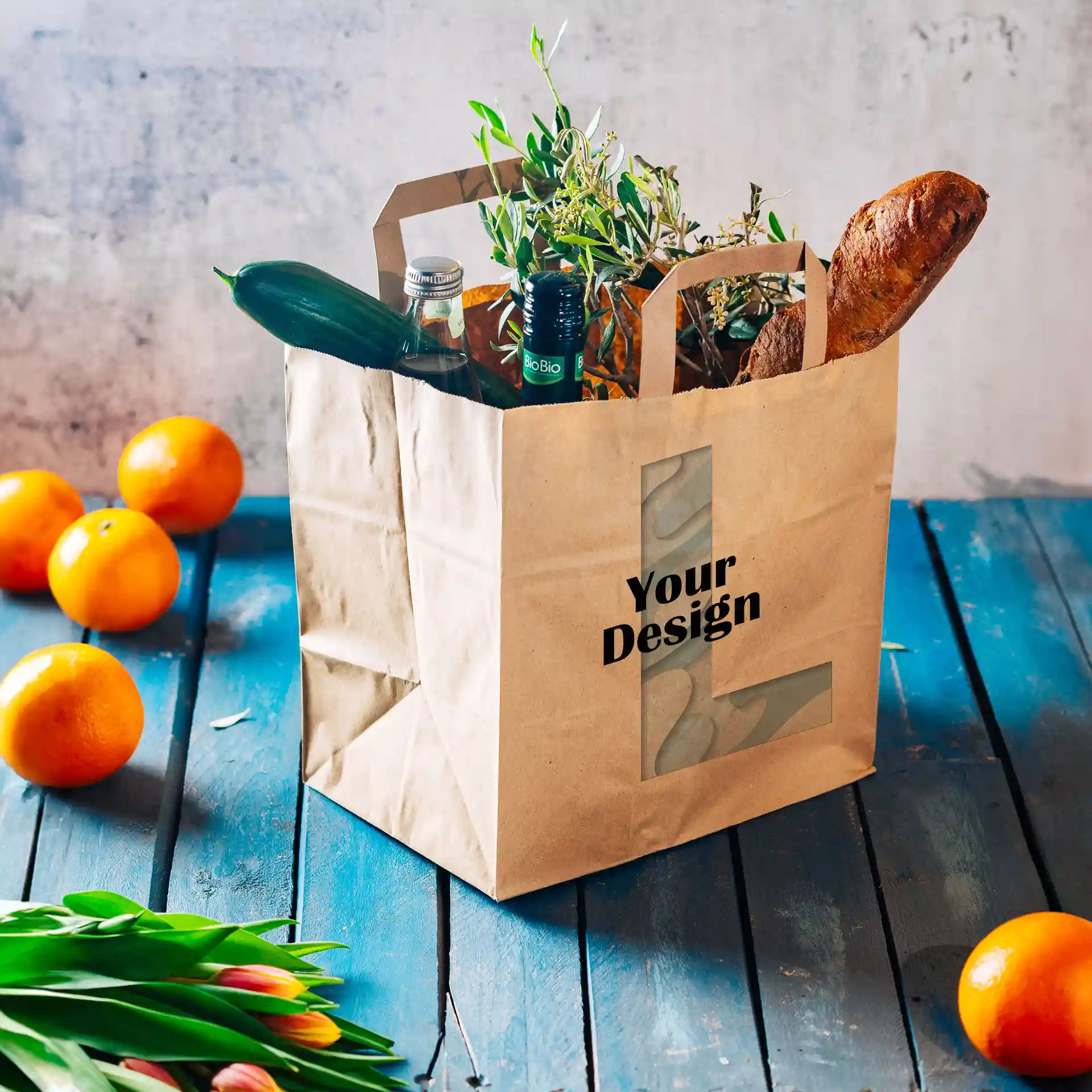 Sac en papier brun à large base, rempli de légumes, de bouteilles et d'une baguette, sur une surface en bois bleu.
