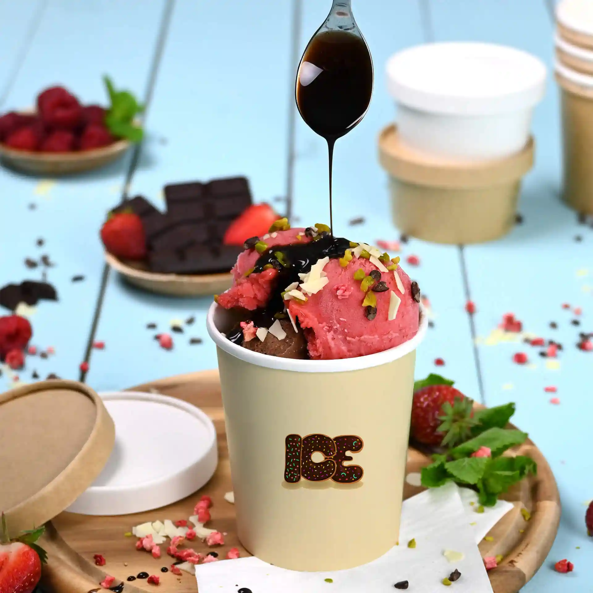 Coupe ronde blanche de glace avec des boules roses et brunes, garnie de sauce au chocolat et de noix, sur un plateau en bois.