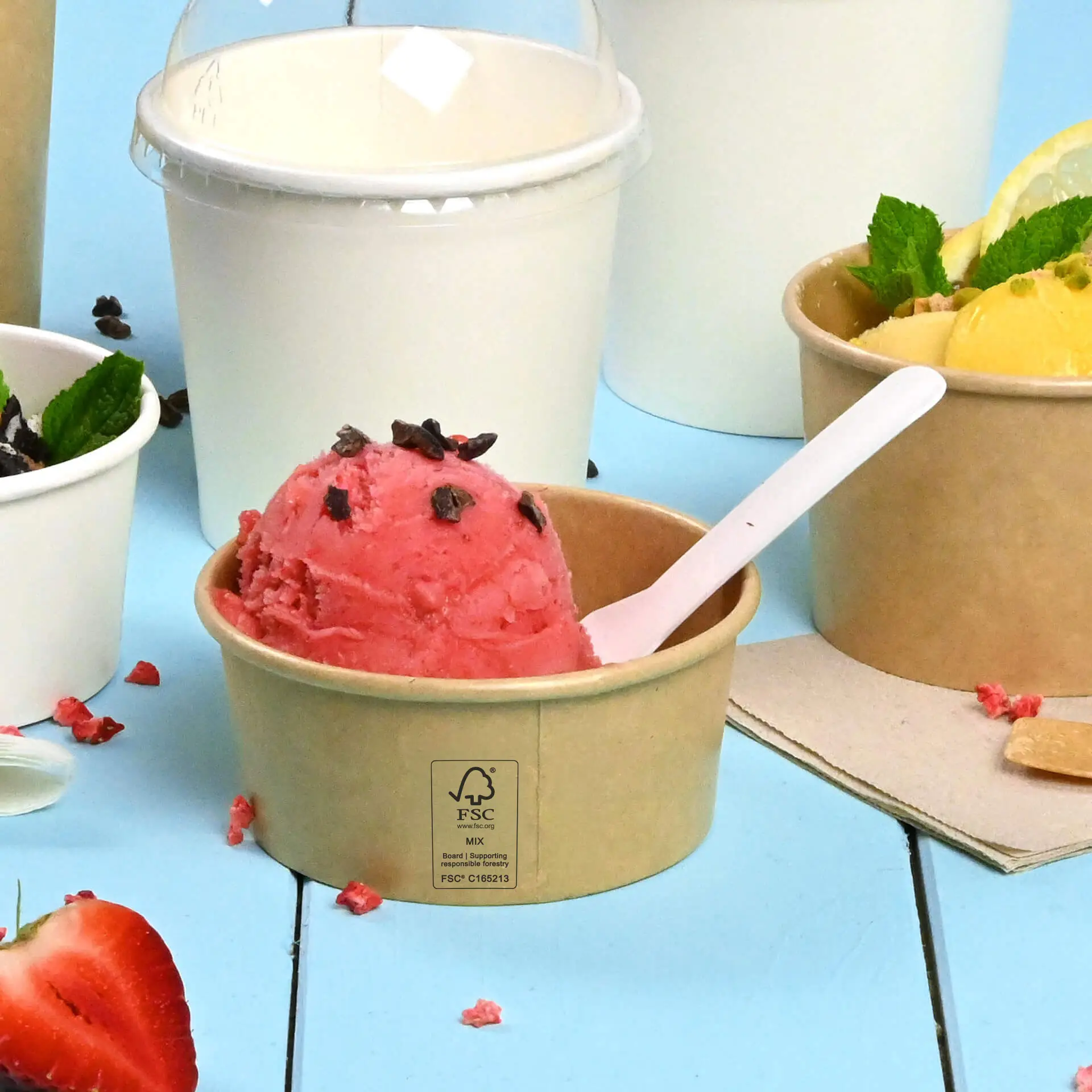 Un gobelet à glace marron, enduit de PE, avec de la glace rose et des vermicelles au chocolat ; d'autres récipients à glace sont partiellement visibles.