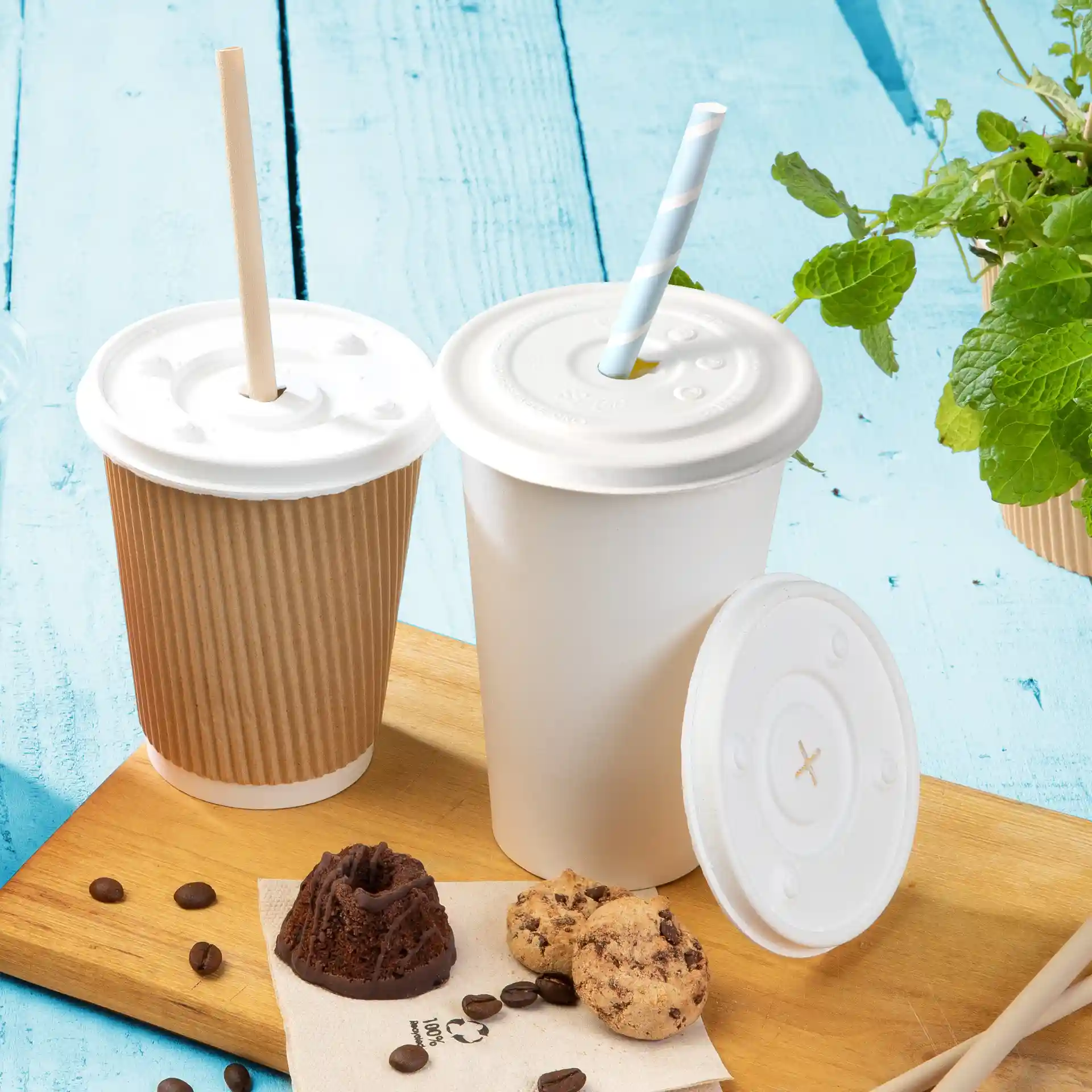 Image de deux gobelets avec des couvercles blancs, l'un avec une paille, placés sur une surface en bois avec des biscuits et des grains de café.