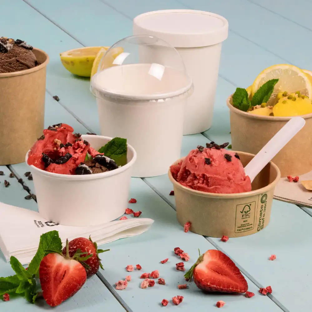 Plusieurs coupes de glace avec des saveurs comme le chocolat et la fraise, garnies de feuilles de menthe, sur une surface en bois bleu.
