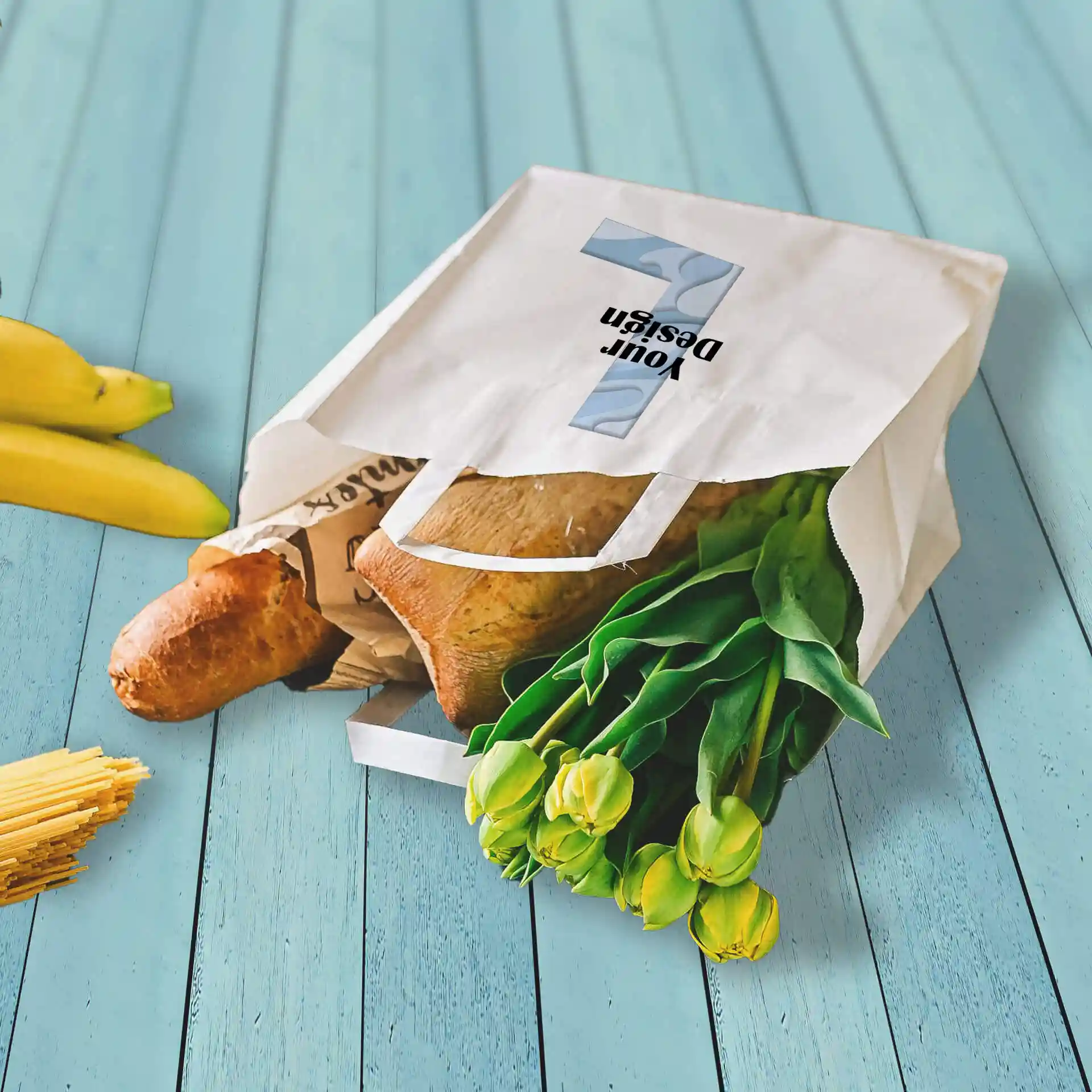 Sac en papier blanc avec des courses, incluant une baguette et des tulipes, sur une surface en bois bleu.