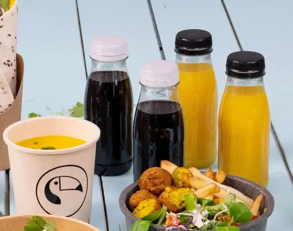 Éléments alimentaires assortis, y compris des bouteilles en plastique rPET avec diverses boissons, un bol de soupe et un saladier, frites et falafel.