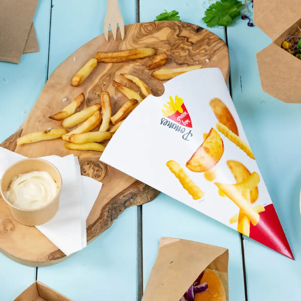 Cornet en papier avec des frites et des quartiers de pommes de terre ; portion de sauce à tremper et frites éparpillées sur une planche en bois.