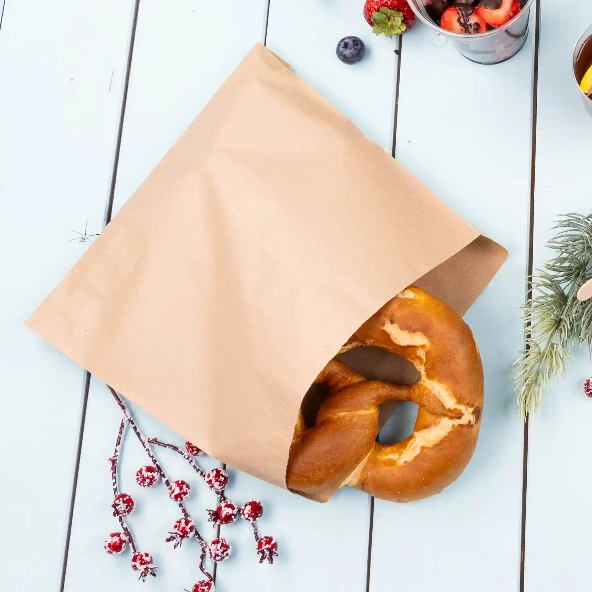 Sac en papier kraft marron partiellement ouvert avec un bretzel visible à l'intérieur, posé sur une surface en bois bleu clair.