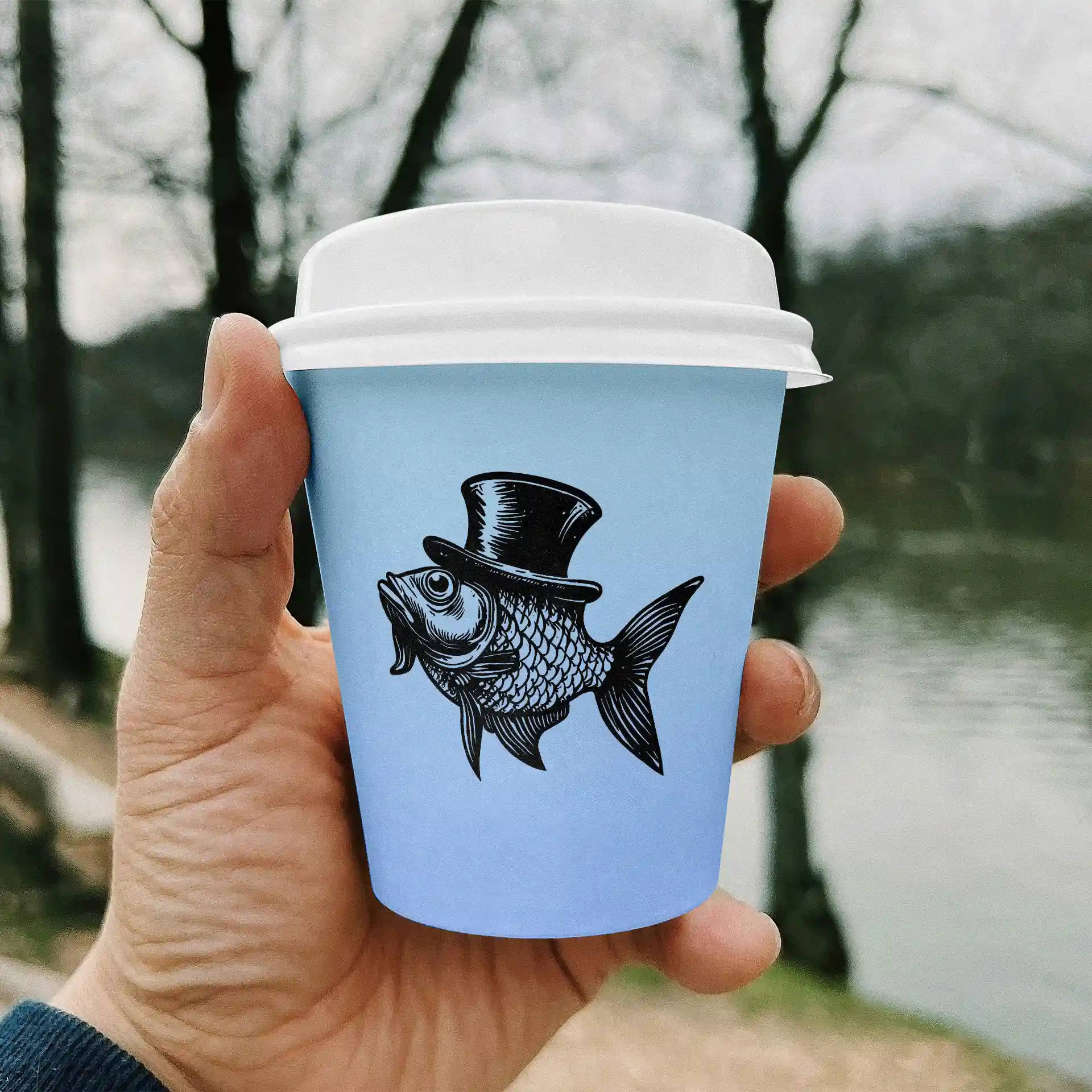Main tenant un gobelet en papier bleu clair avec une illustration noire d'un poisson portant un haut-de-forme, avec un arrière-plan flou.