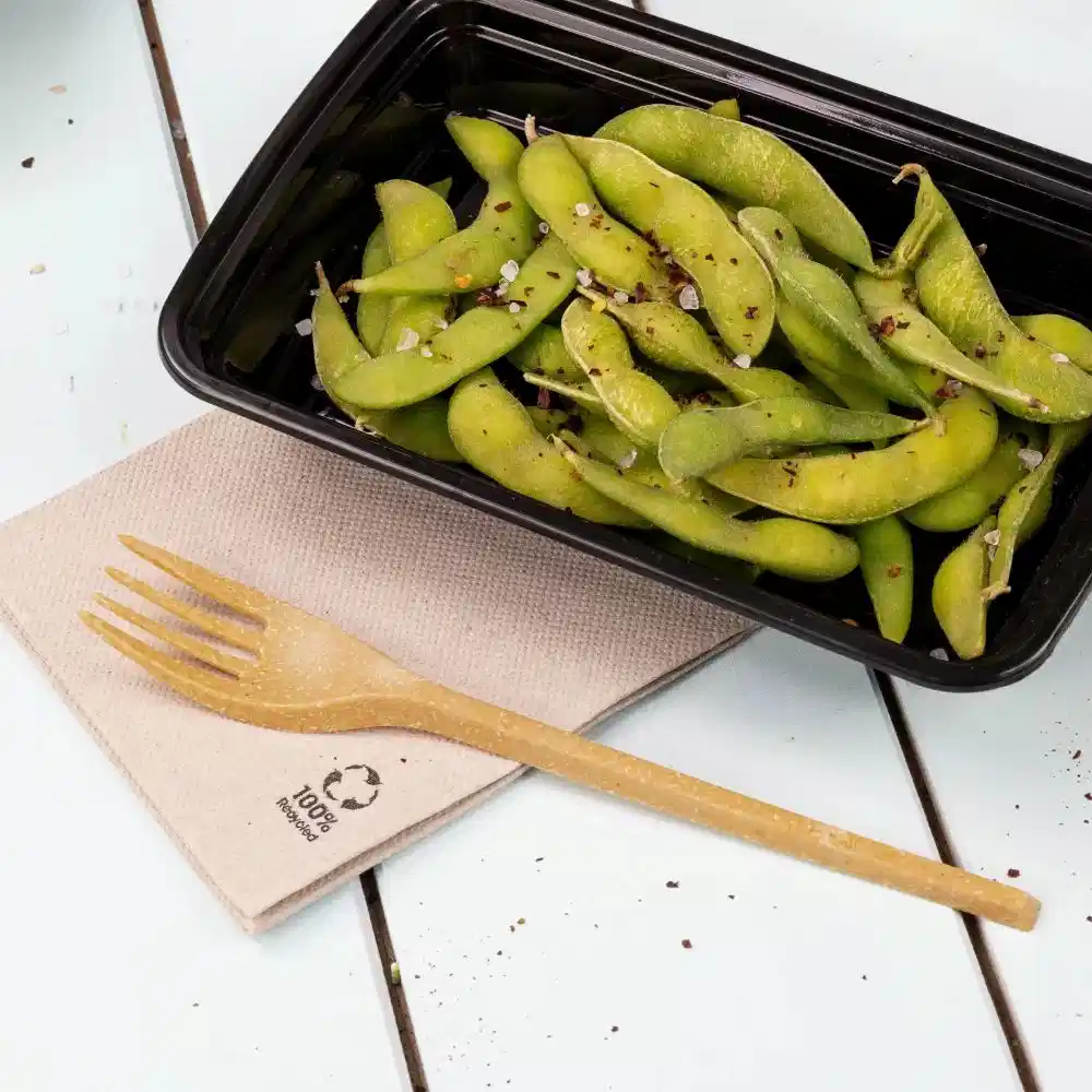 Contenant de fèves edamame saupoudrées d'épices, à côté d'une fourchette en bois sur une serviette texturée.