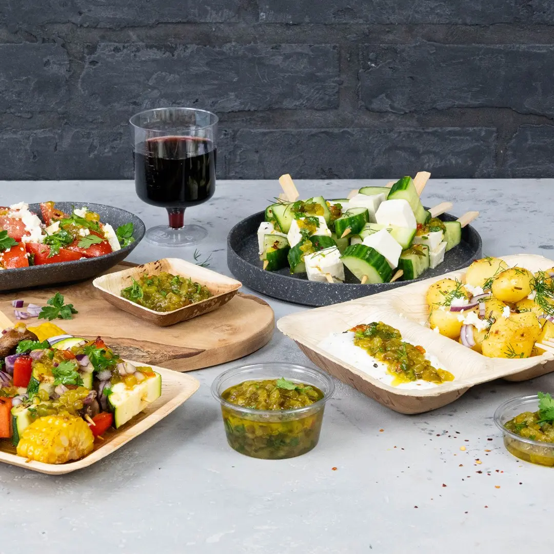Une variété de finger foods incluant des salades, des brochettes de concombre et de fromage, et des sauces, avec un verre de vin rouge en arrière-plan.