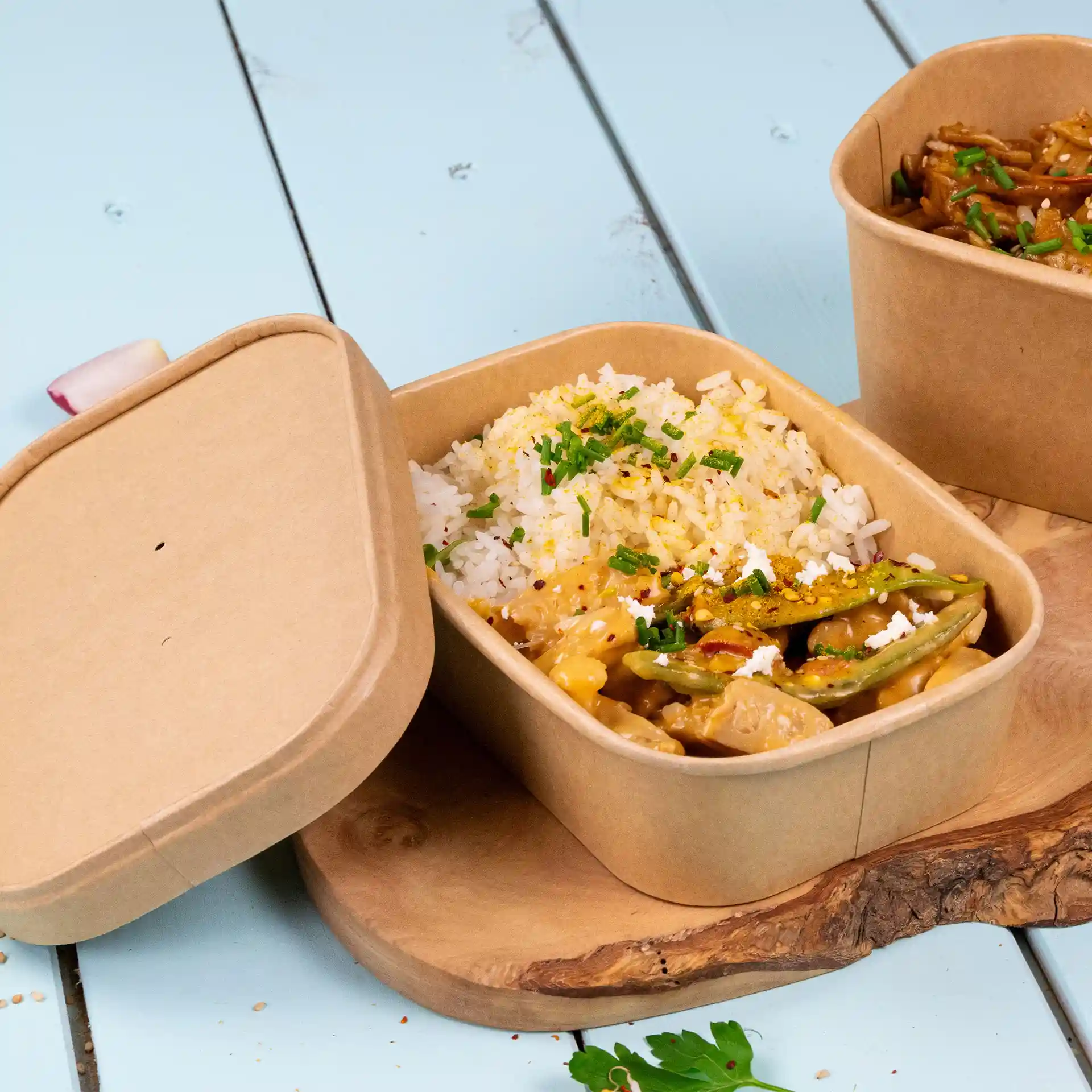 Conteneur alimentaire en kraft rectangulaire avec du riz et des légumes, partiellement ouvert, sur une surface en bois.