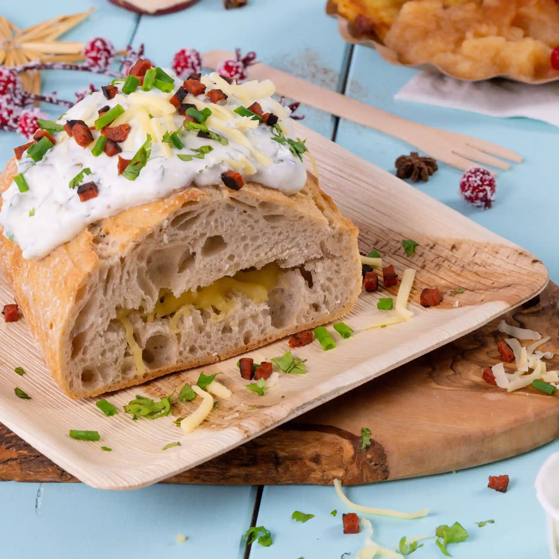 Assiette carrée en feuille de palmier avec un pain coupé garni de sauce, fromage et herbes, sur une surface en bois.