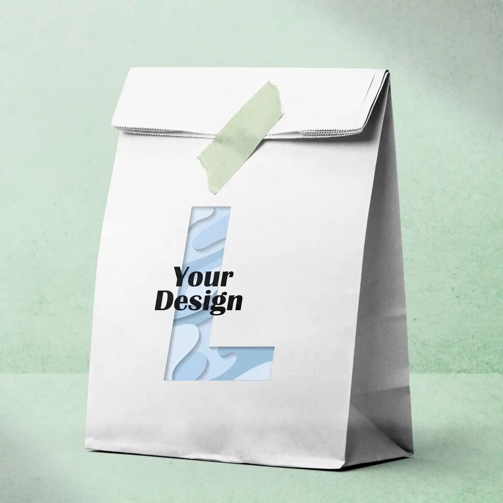Sac en papier blanc imprimé avec une lettre 'L' découpée et le texte 'Votre Design', fixé avec du ruban vert.