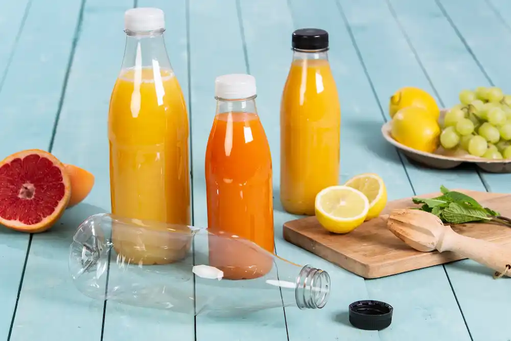 Deux bouteilles en verre remplies de jus d'orange et de jus jaune, un citron coupé, des raisins et une moitié de pamplemousse sur une surface en bois.