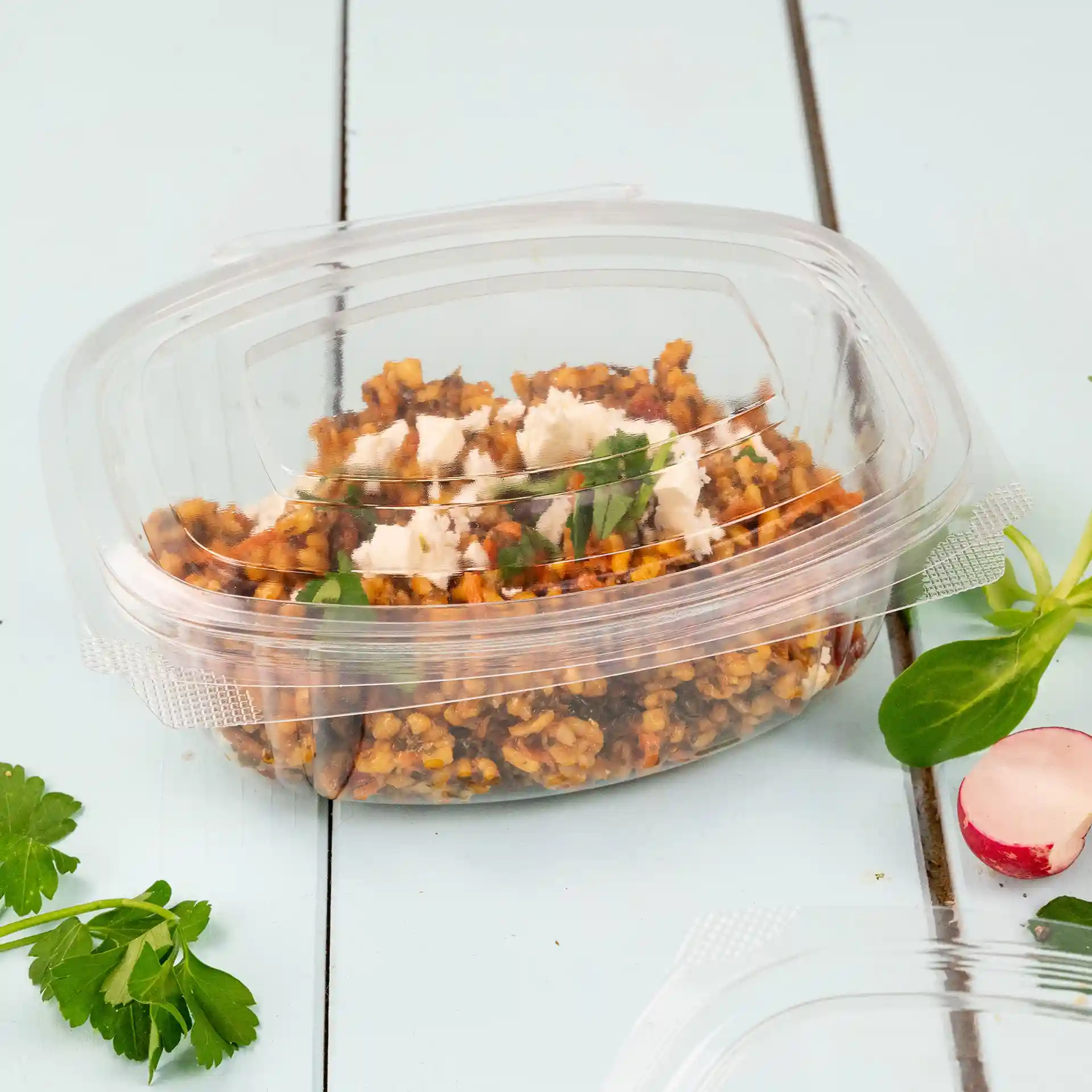 Bol rectangulaire en PLA transparent avec un couvercle pliable, contenant un mélange alimentaire et garni d'herbes.