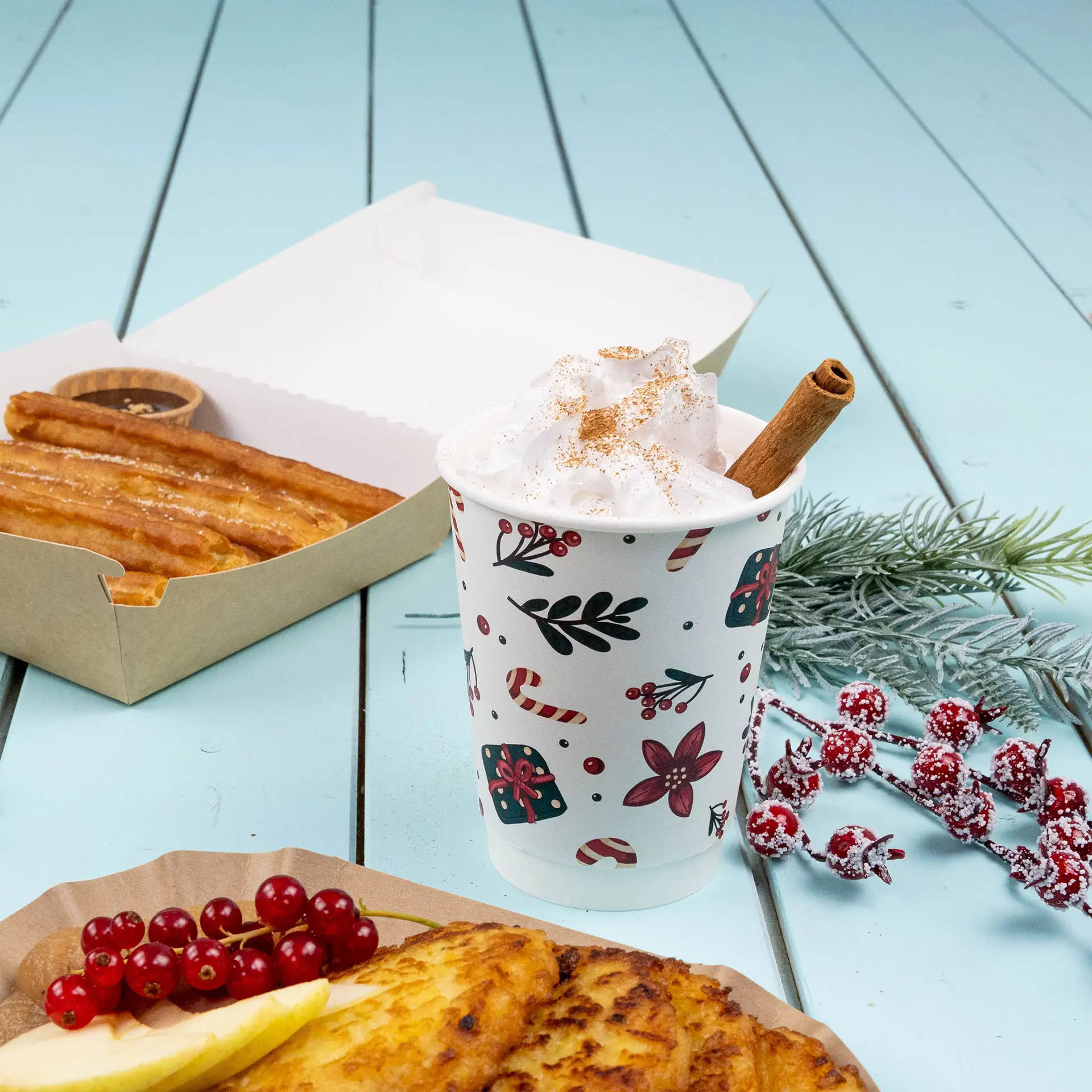 Tasse double paroi avec design d'hiver, remplie de crème fouettée et d'un bâton de cannelle, accompagnée de churros et de fruits.