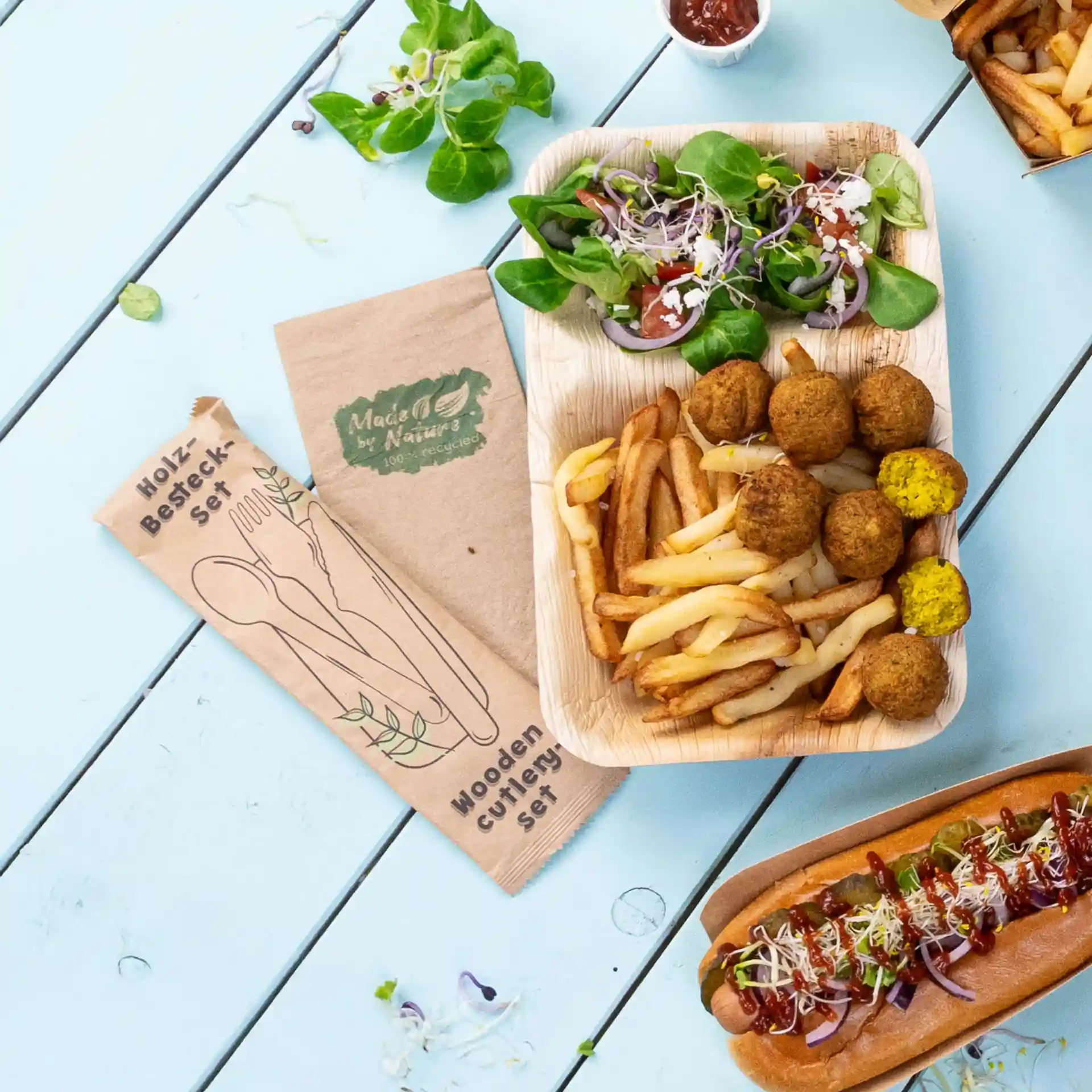 Image d'un ensemble de couverts en bois avec un couteau, une fourchette et une cuillère, à côté d'une assiette de frites, falafels et salade.