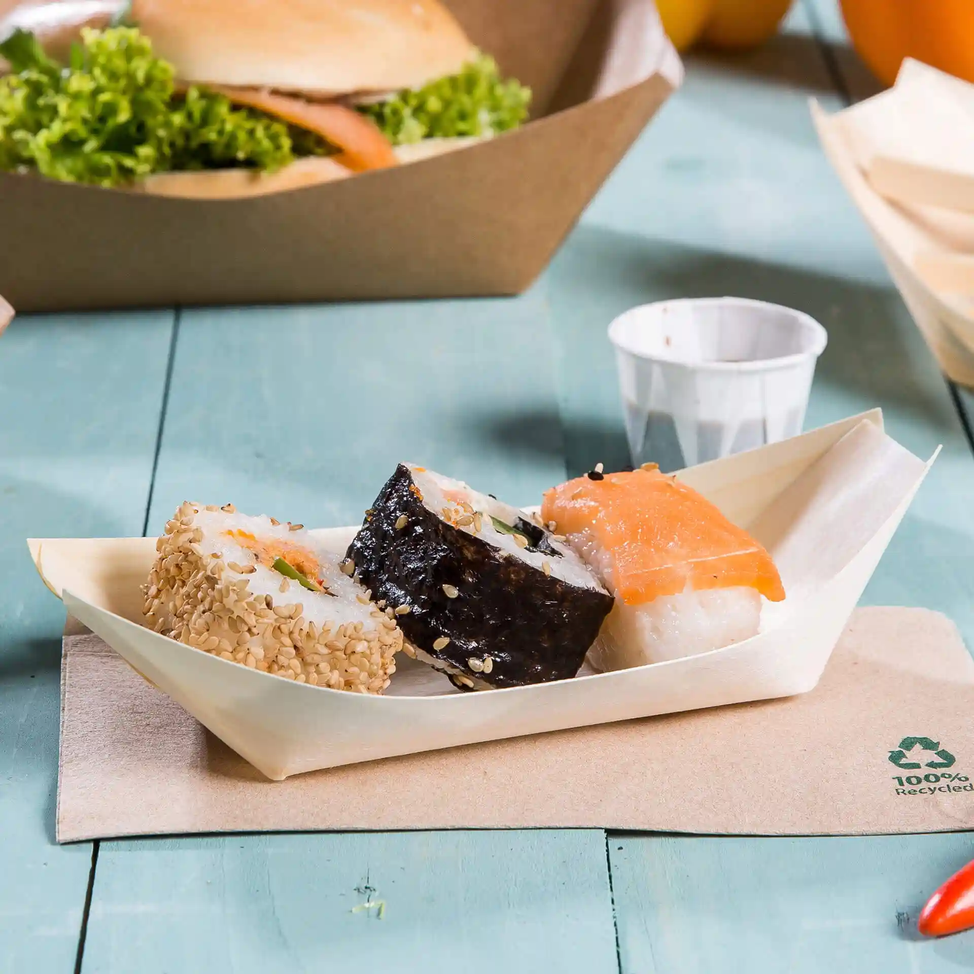 Trois pièces de sushi servies dans un plateau en bois en forme de bateau sur une surface bleu clair.