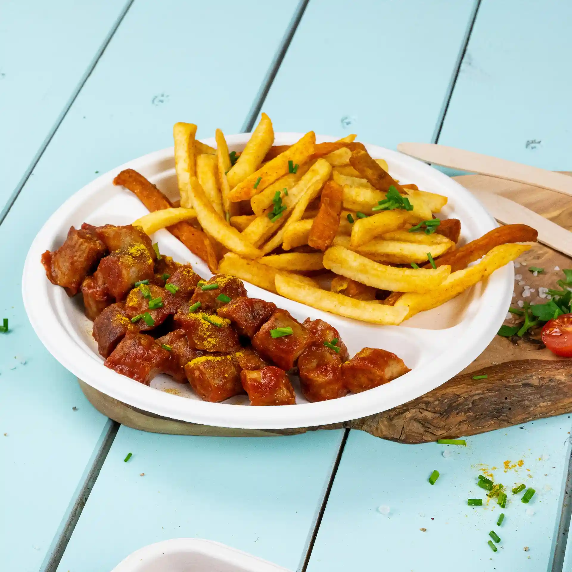 Assiette ronde en canne à sucre blanche avec deux compartiments, l'un rempli de viande en dés dans une sauce et l'autre de frites.