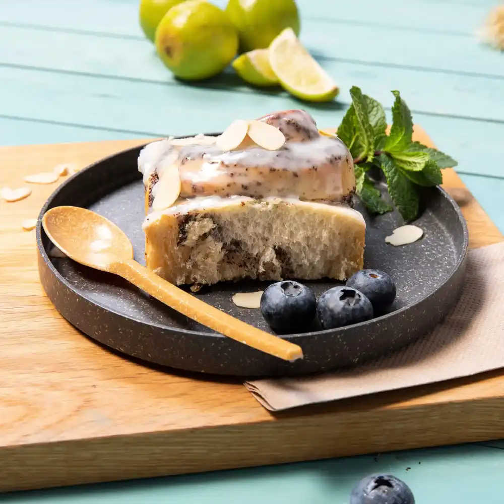 Part de dessert sur une assiette sombre avec des myrtilles, des amandes, une cuillère en bois et des feuilles de menthe fraîches.