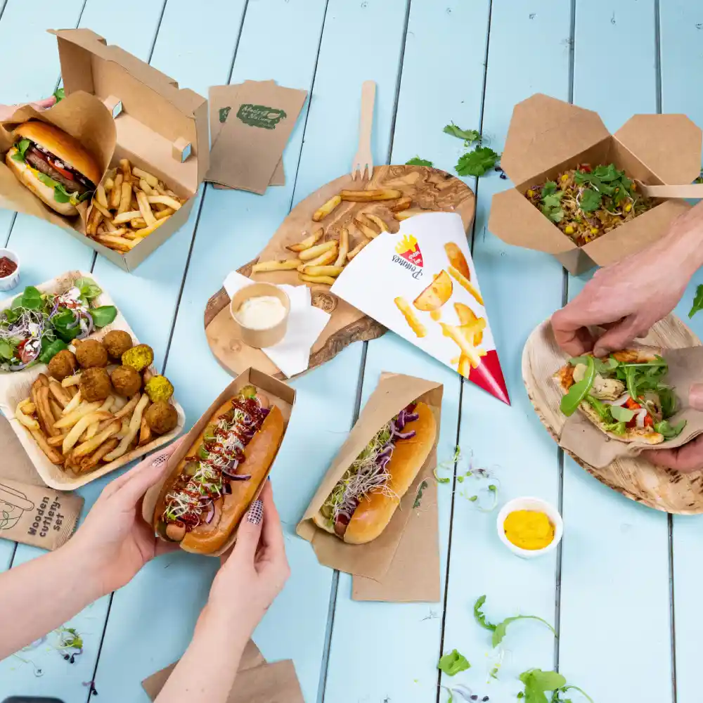 Une variété d'aliments, y compris des hot-dogs, des frites, des salades et une sauce à tremper sur une table en bois bleue.