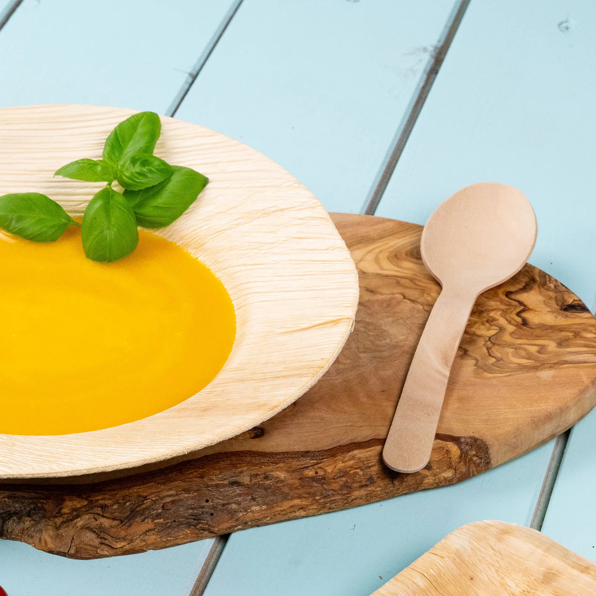 Bol avec de la soupe jaune et une feuille de basilic, accompagné d'une cuillère en bois sur une planche en bois.