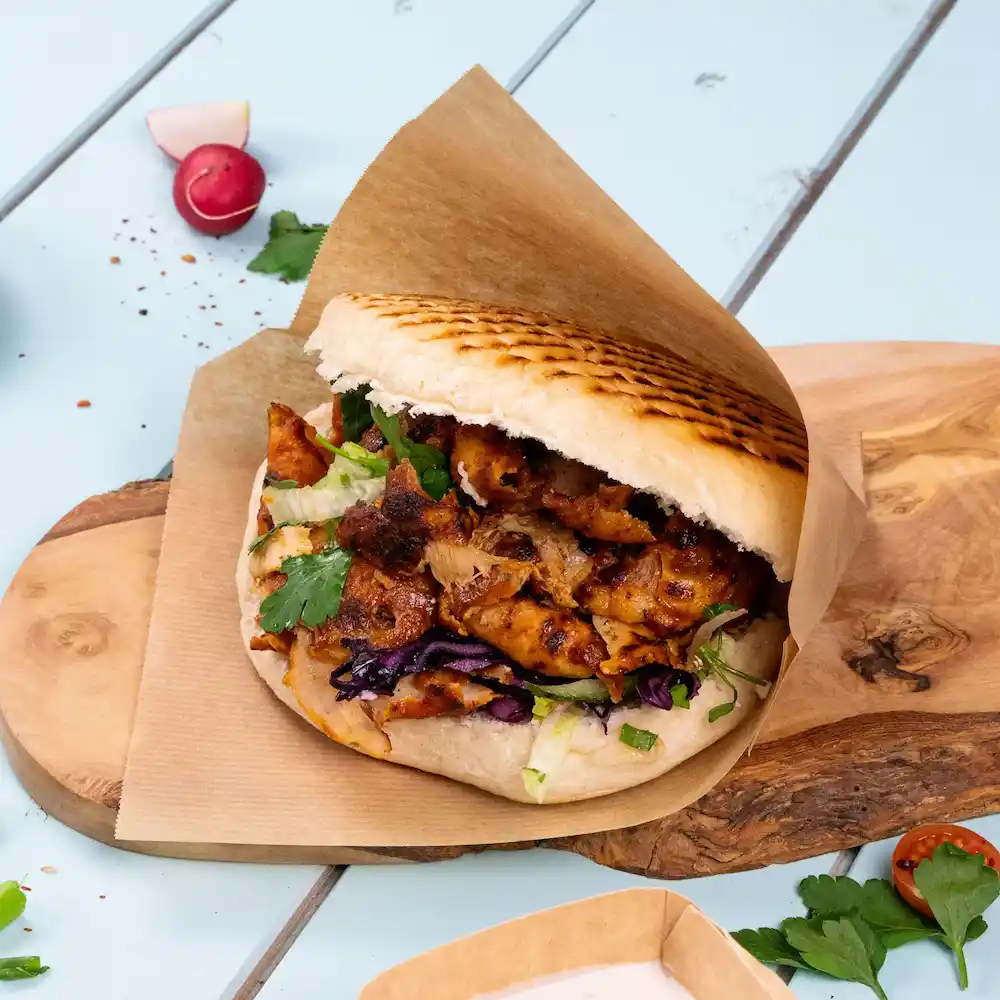 Un sandwich pita garni avec du poulet grillé, de la laitue, du chou rouge et de la coriandre sur une planche en bois.