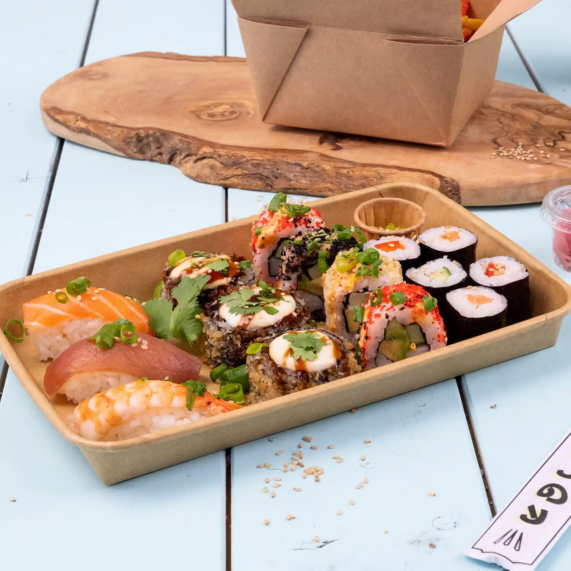 Assortiment de sushi dans une boîte en PE brun, avec divers rouleaux et sashimi sur une surface en bois bleu.