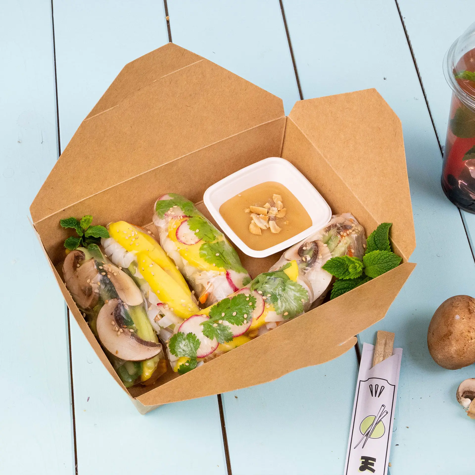 Bocaux alimentaires à emporter bruns, capacité de 1100 ml, avec des baguettes et des aliments ; emballage biodégradable sur une surface bleu clair.