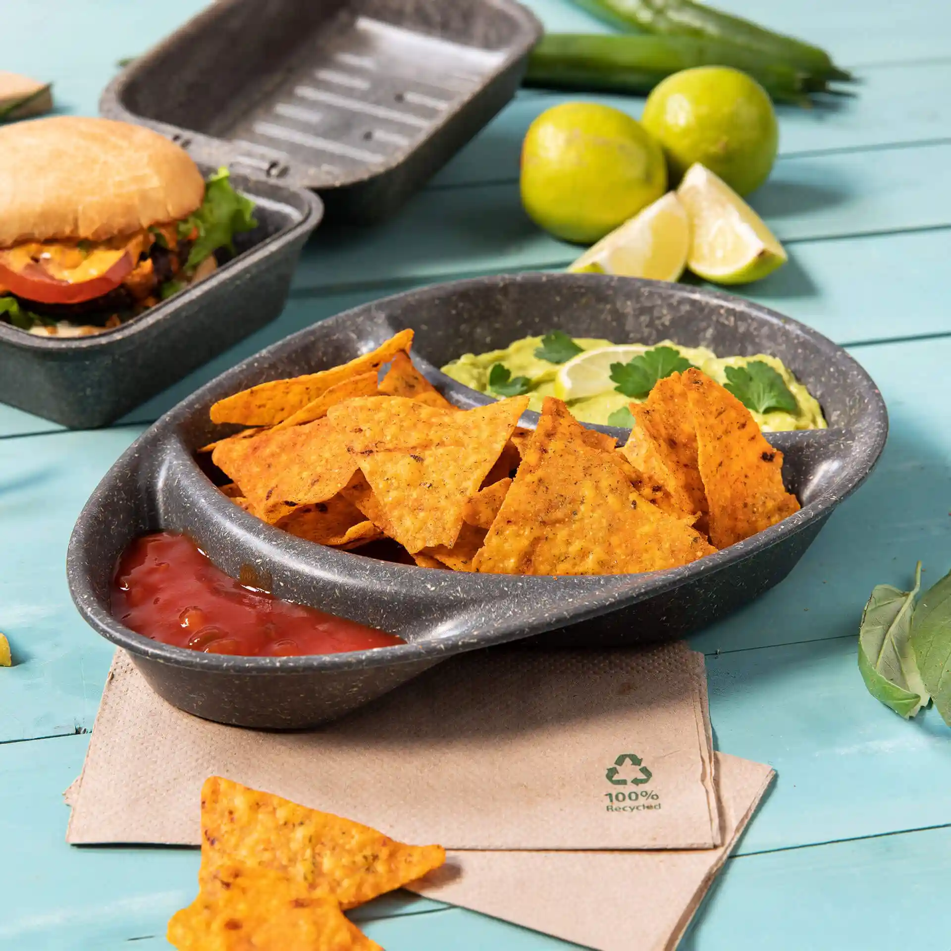 Assiette divisée réutilisable avec trois compartiments, remplie de nachos, salsa et guacamole, sur une surface bleue.
