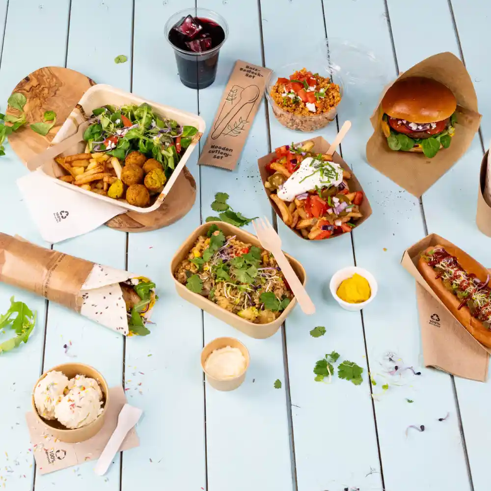 Disposition de divers plats de restauration sur une table bleu clair, incluant salades, burgers, hot-dogs et desserts. Une boisson est également incluse.