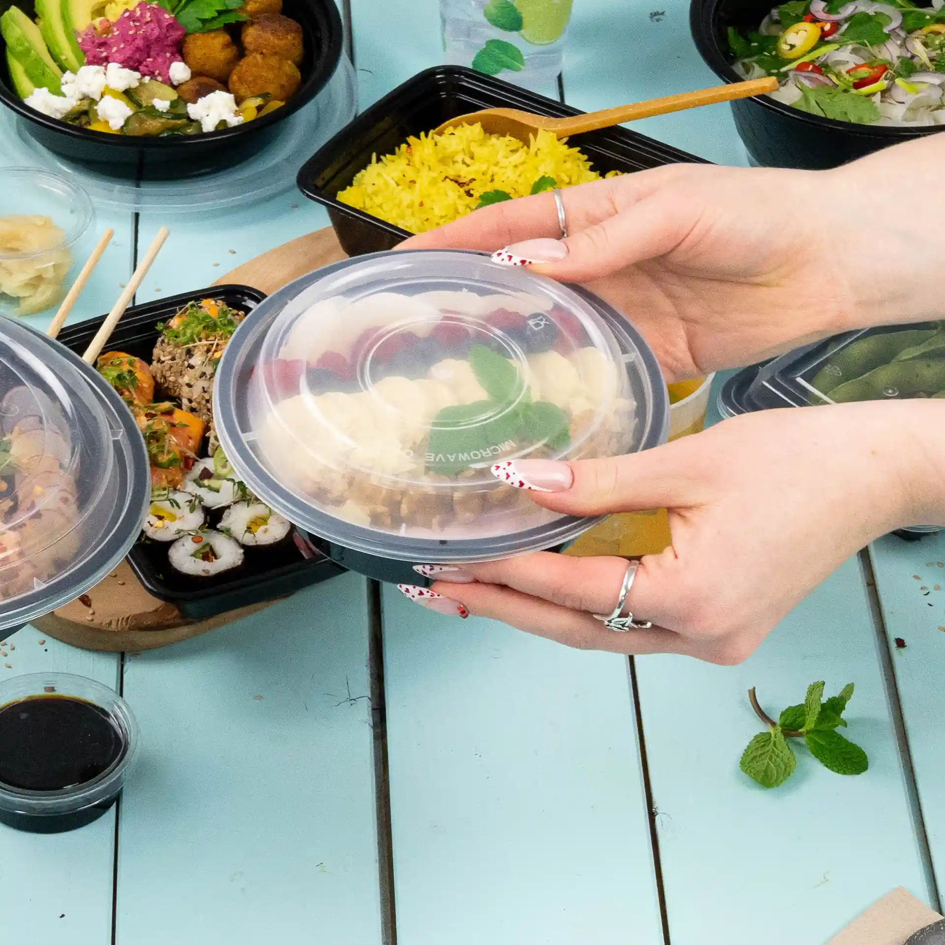 Couvercle rond réutilisable transparent en PP, tenu au-dessus d'une table avec divers contenants alimentaires.
