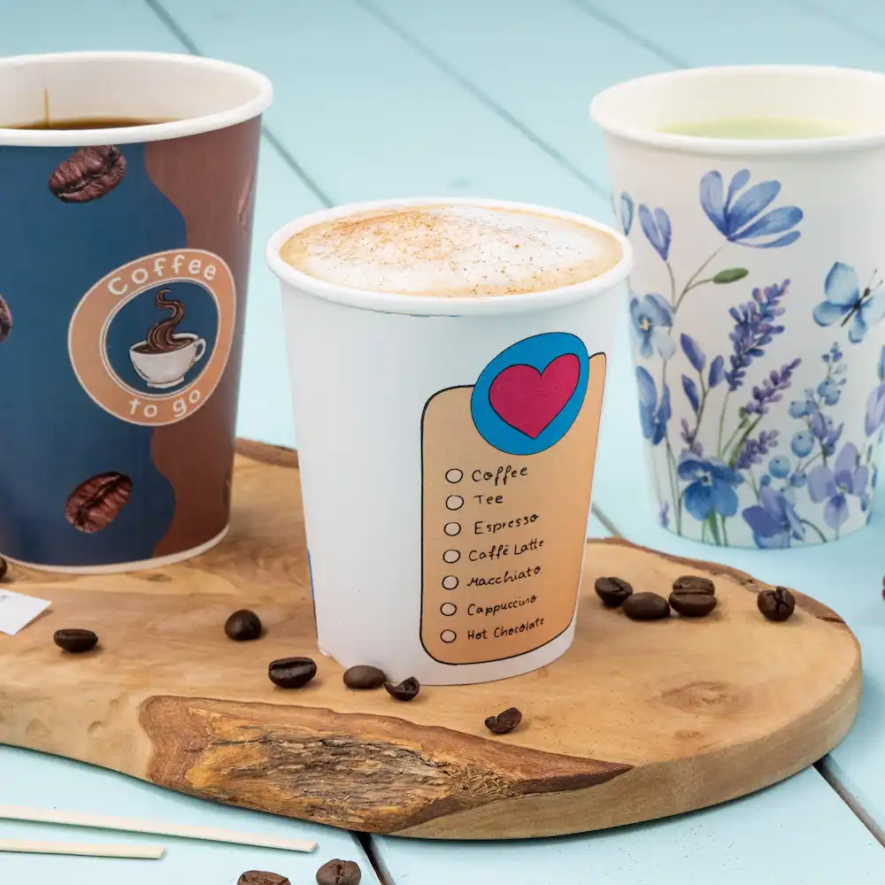 Trois gobelets en papier remplis de boissons, dont un gobelet de café avec une liste de choix de boissons, sur une surface en bois.