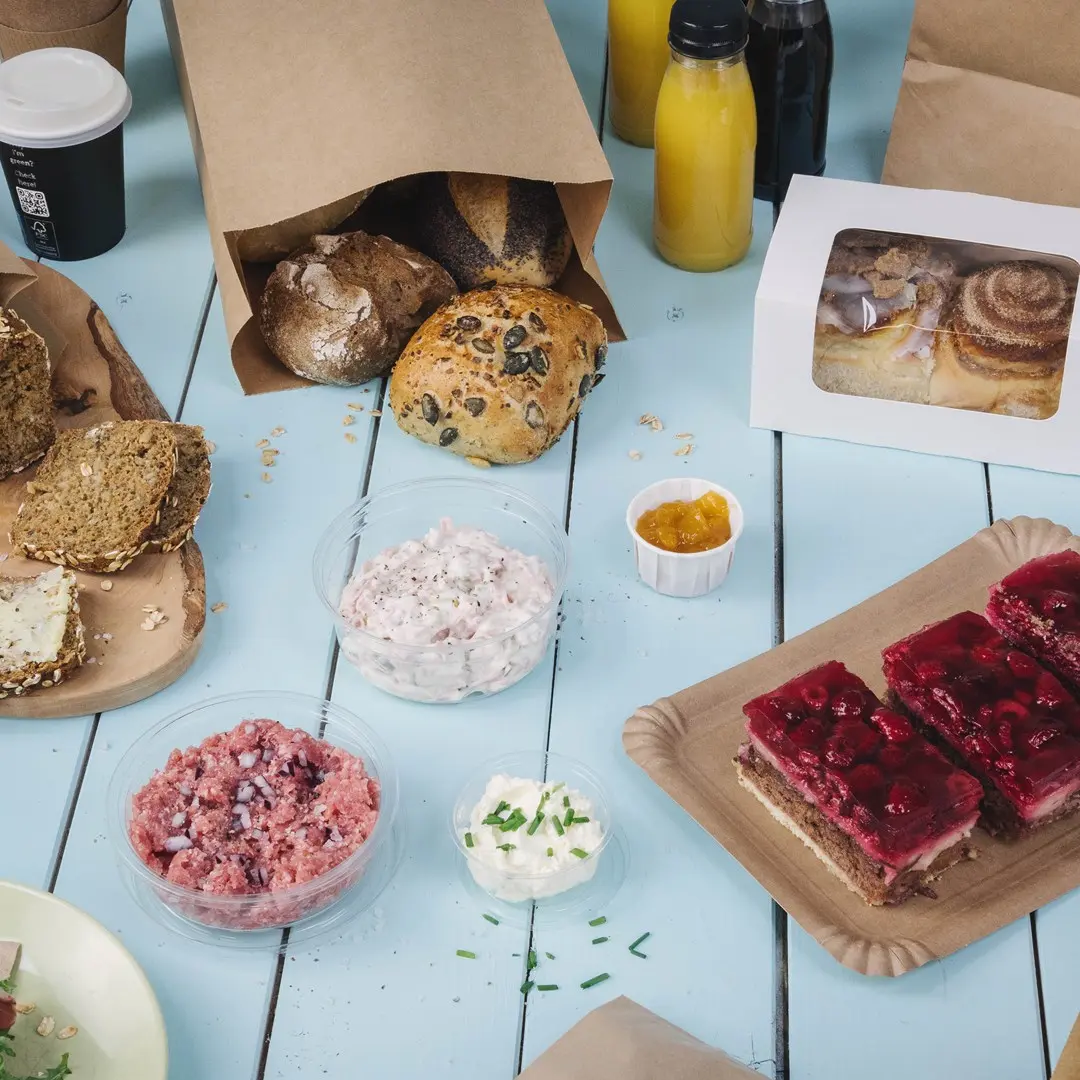 Assortiment de produits de boulangerie, desserts et dips sur une table en bois bleue, avec des boissons en arrière-plan.