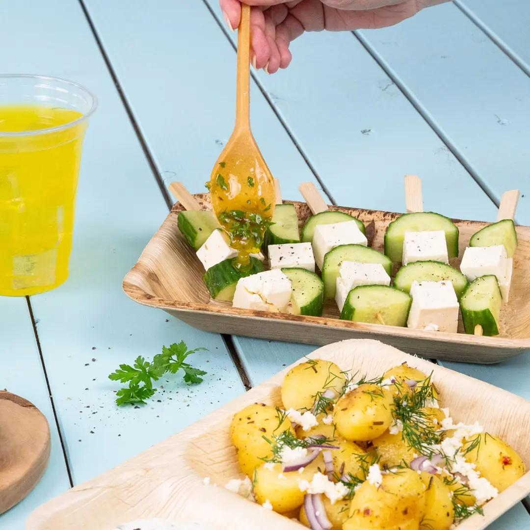 Brochettes en bois avec concombre et cubes de fromage, servies avec des pommes de terre assaisonnées et une boisson.