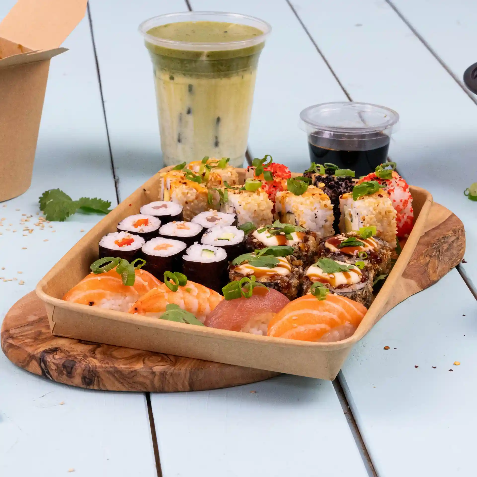Plateau de sushis assortis, y compris des crevettes et du saumon, avec une boisson et une sauce d'accompagnement sur une planche en bois.