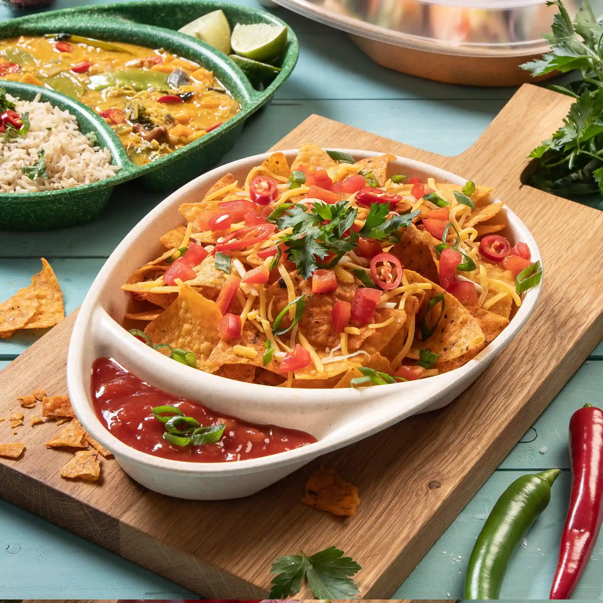 Plat avec des nachos garnis de fromage, tomates et coriandre, servi avec de la salsa dans une assiette blanche divisée.
