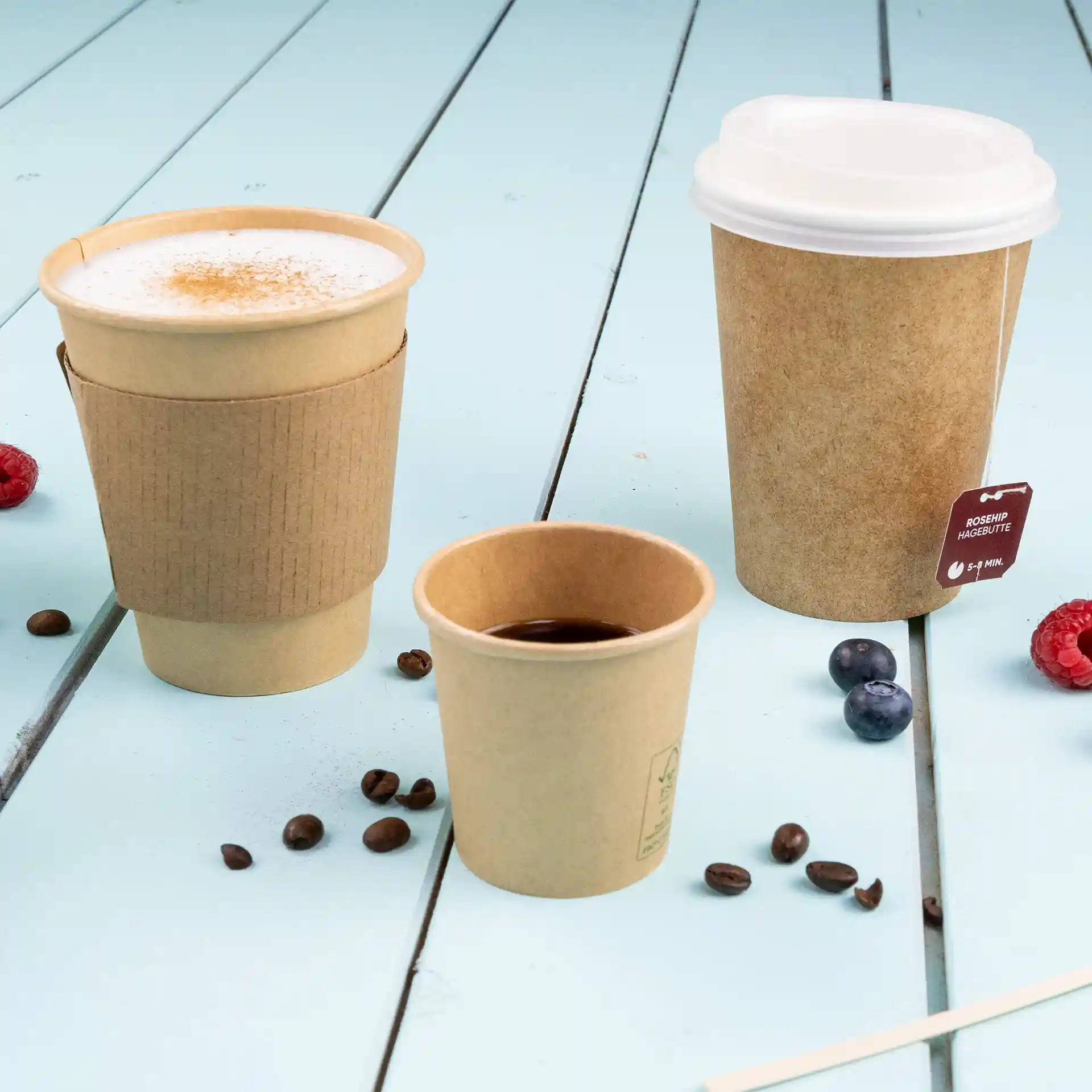 Image de trois gobelets en papier brun sur une surface en bois bleu, incluant un gobelet de 200 ml avec manchon, un plus petit gobelet et un couvercle.