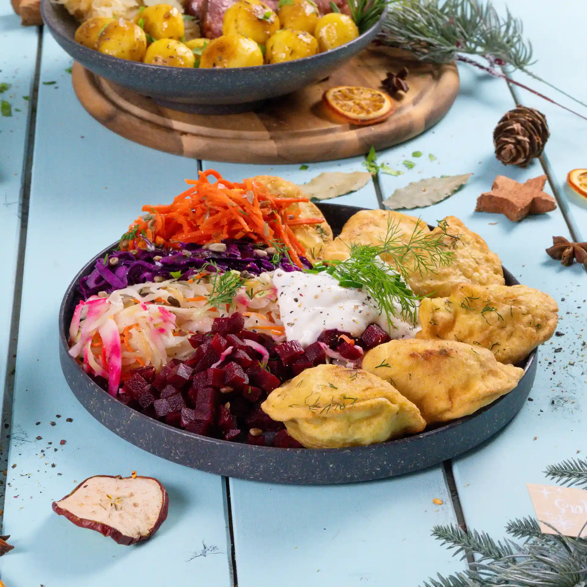 Assiette ronde grise réutilisable remplie de diverses salades colorées, dips et aliments frits, placée sur une surface bleue.