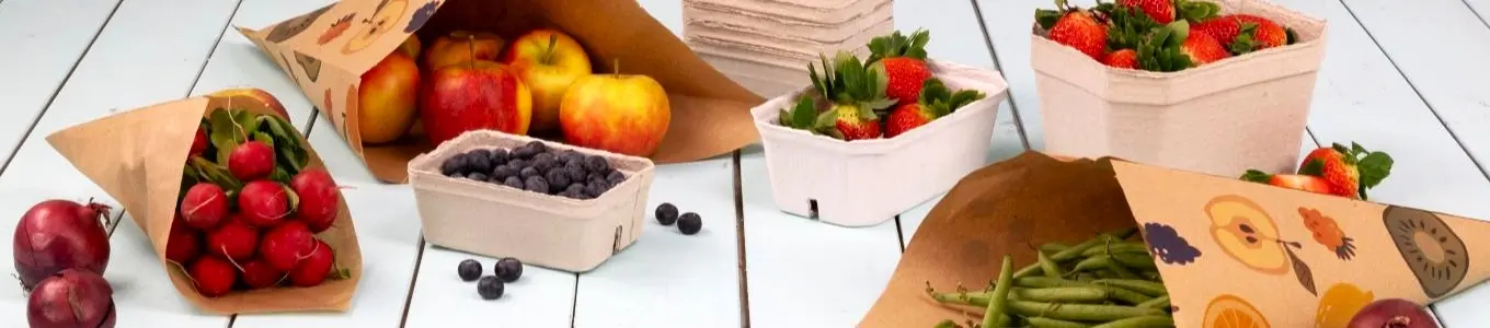 Fruits et légumes variés dans des cônes et contenants en papier sur une surface en bois clair.