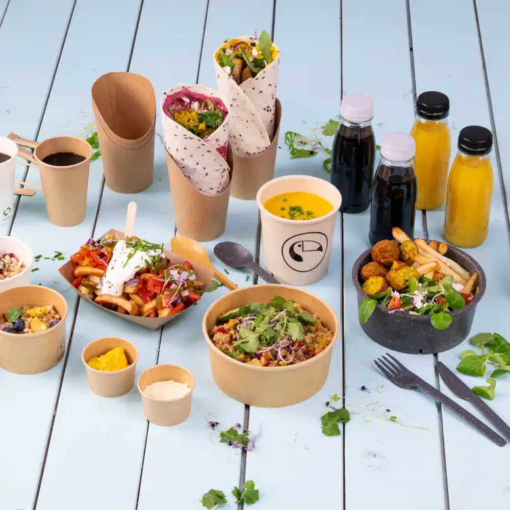 Articles alimentaires variés dans un emballage écologique, y compris des wraps, des salades, des soupes et des boissons sur une surface en bois bleue.