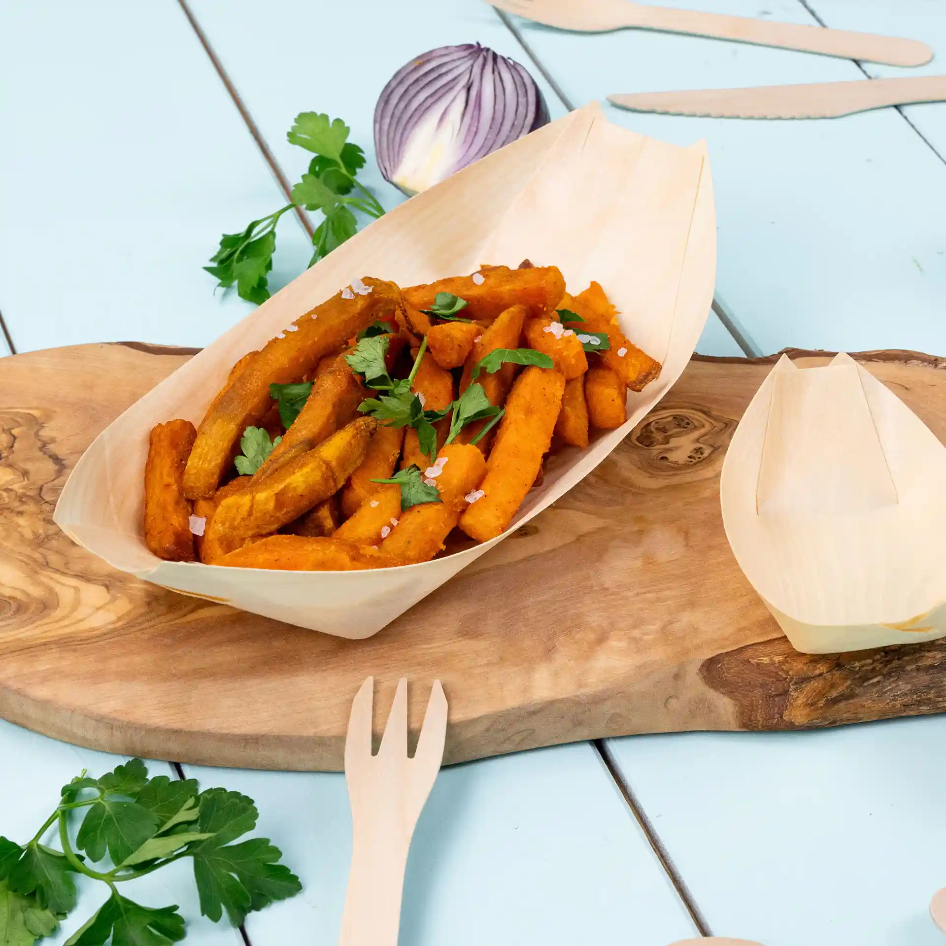 Plat en forme de bateau en bois avec des frites de patate douce, garni de persil, sur une surface en bois.