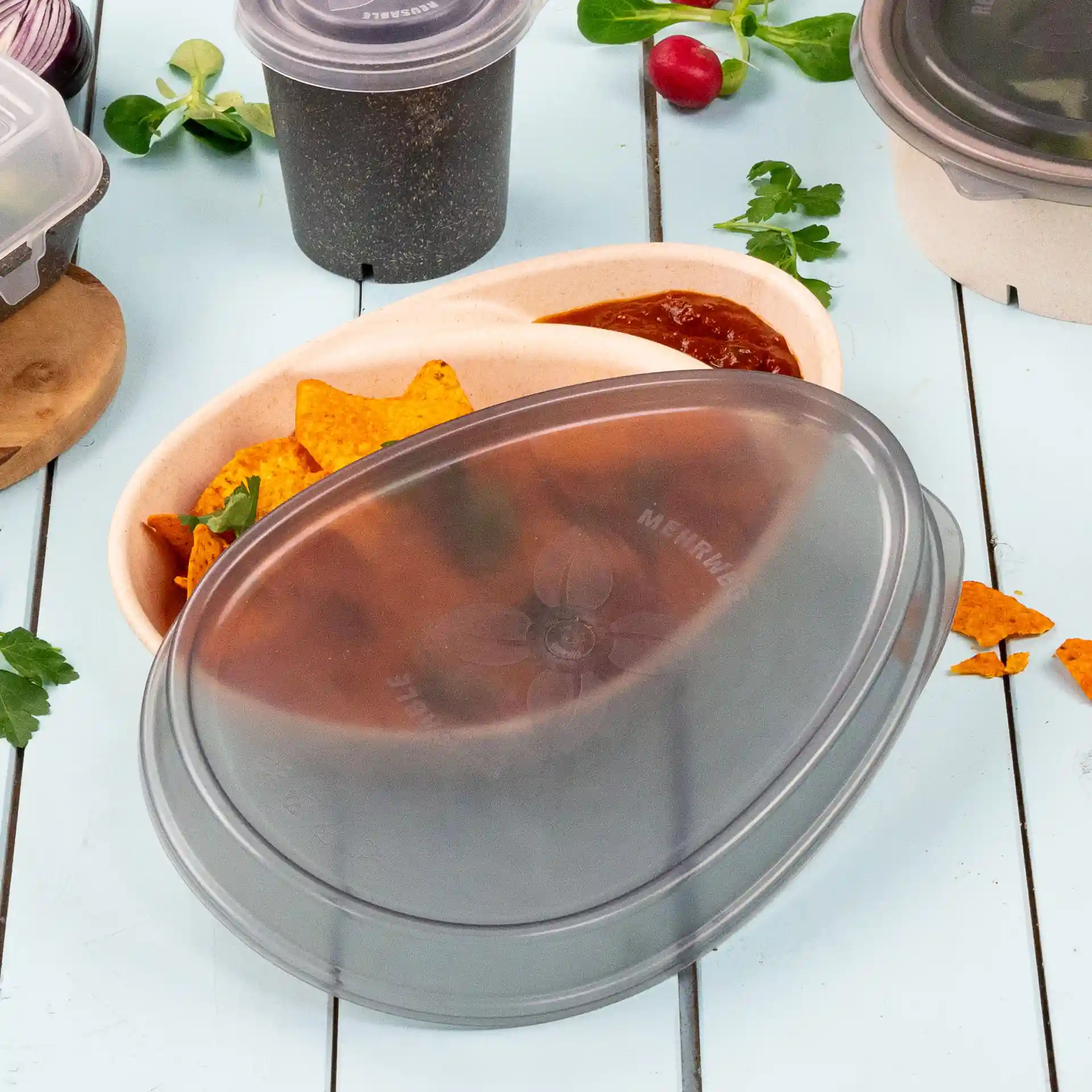 Couvercle réutilisable ovale gris pour une assiette, présenté avec des chips tortilla et de la salsa dans un contenant, sur une surface bleu clair.