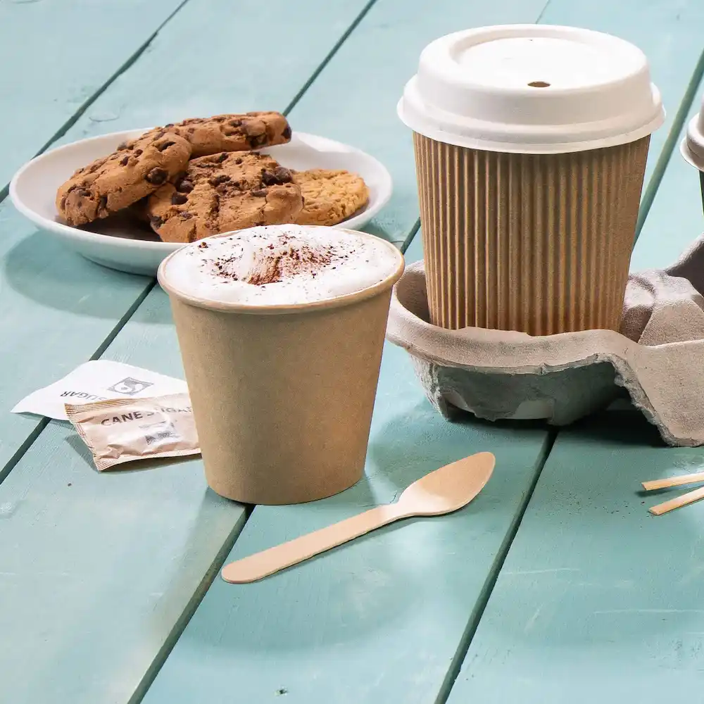 Tasse à café marron avec mousse et cacao, assiette à biscuits, cuillère en bois et porte-tasse sur une surface en bois bleu.