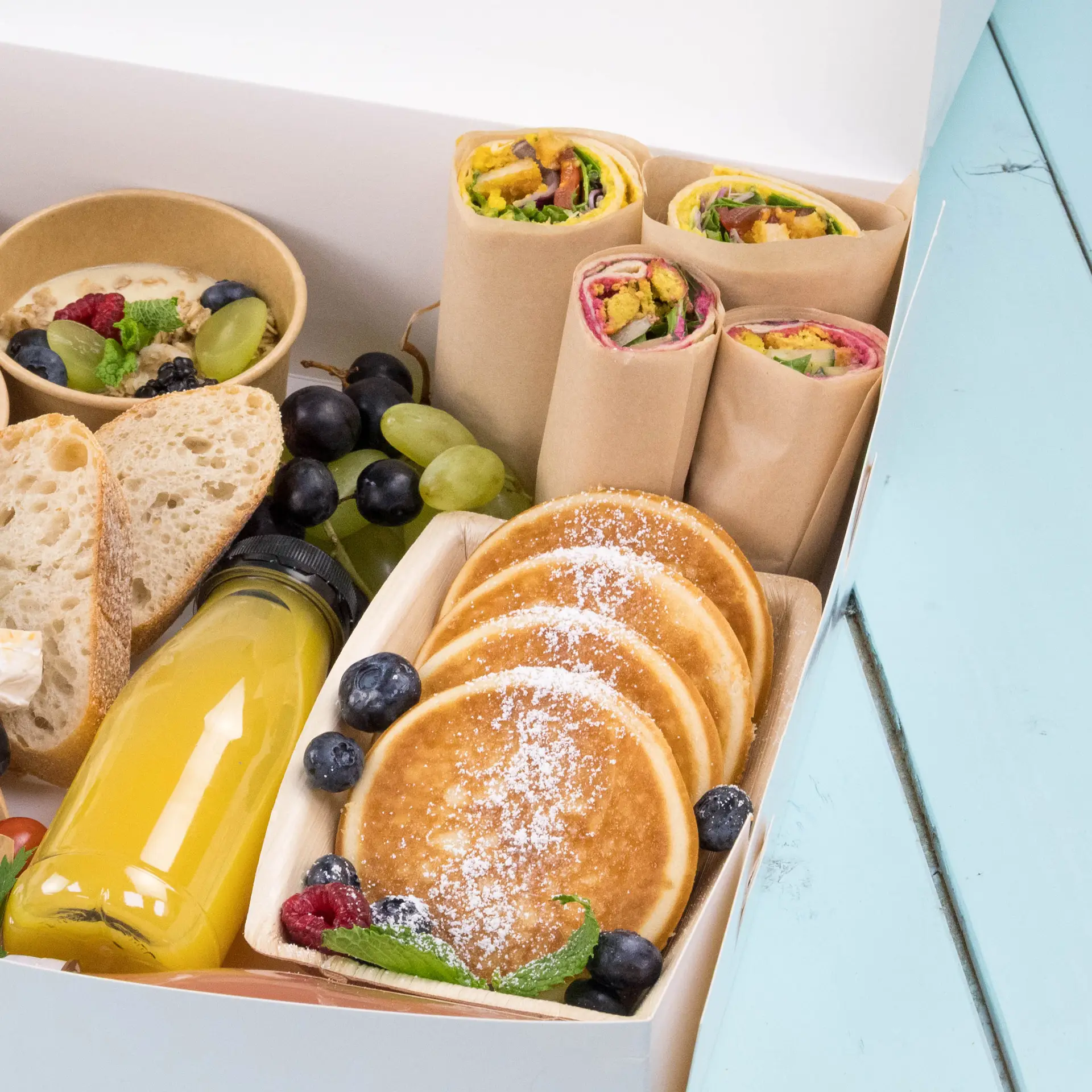 Plateau avec des crêpes, wraps de légumes, fruits, pain et une bouteille de jus pour un usage en restauration.