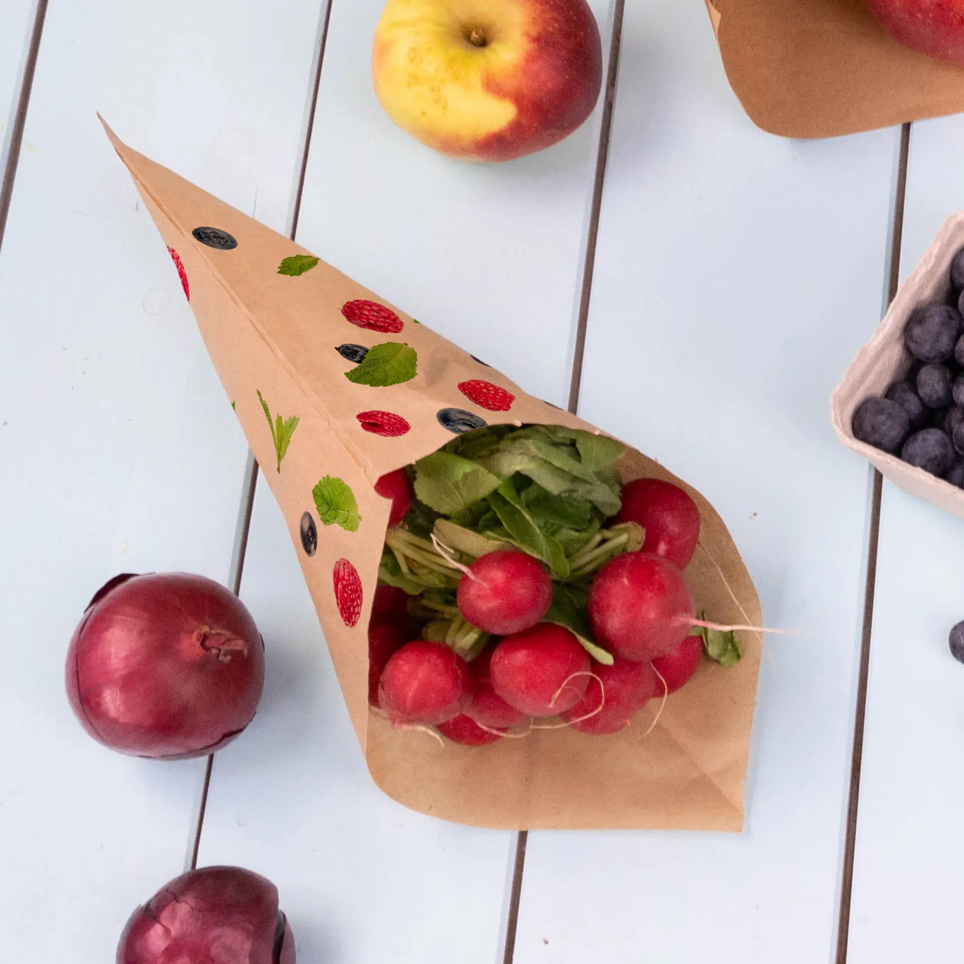 Sac cone en papier brun rempli de radis et d'herbes, entouré de pommes, d'oignons rouges et de myrtilles sur une surface claire.