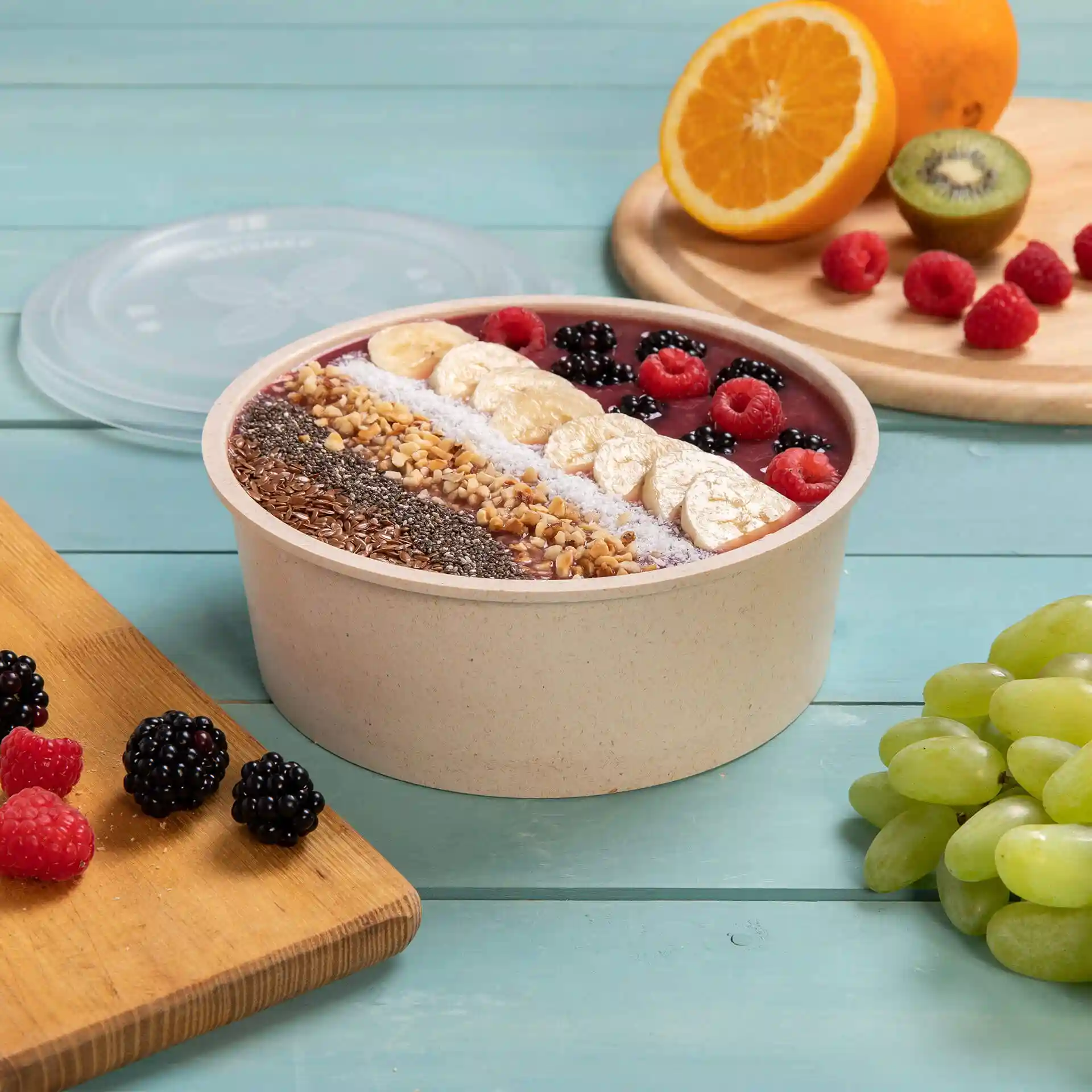 Bol rond réutilisable rempli de smoothie et garni de fruits, placé sur une surface en bois bleu avec des fruits supplémentaires à proximité.
